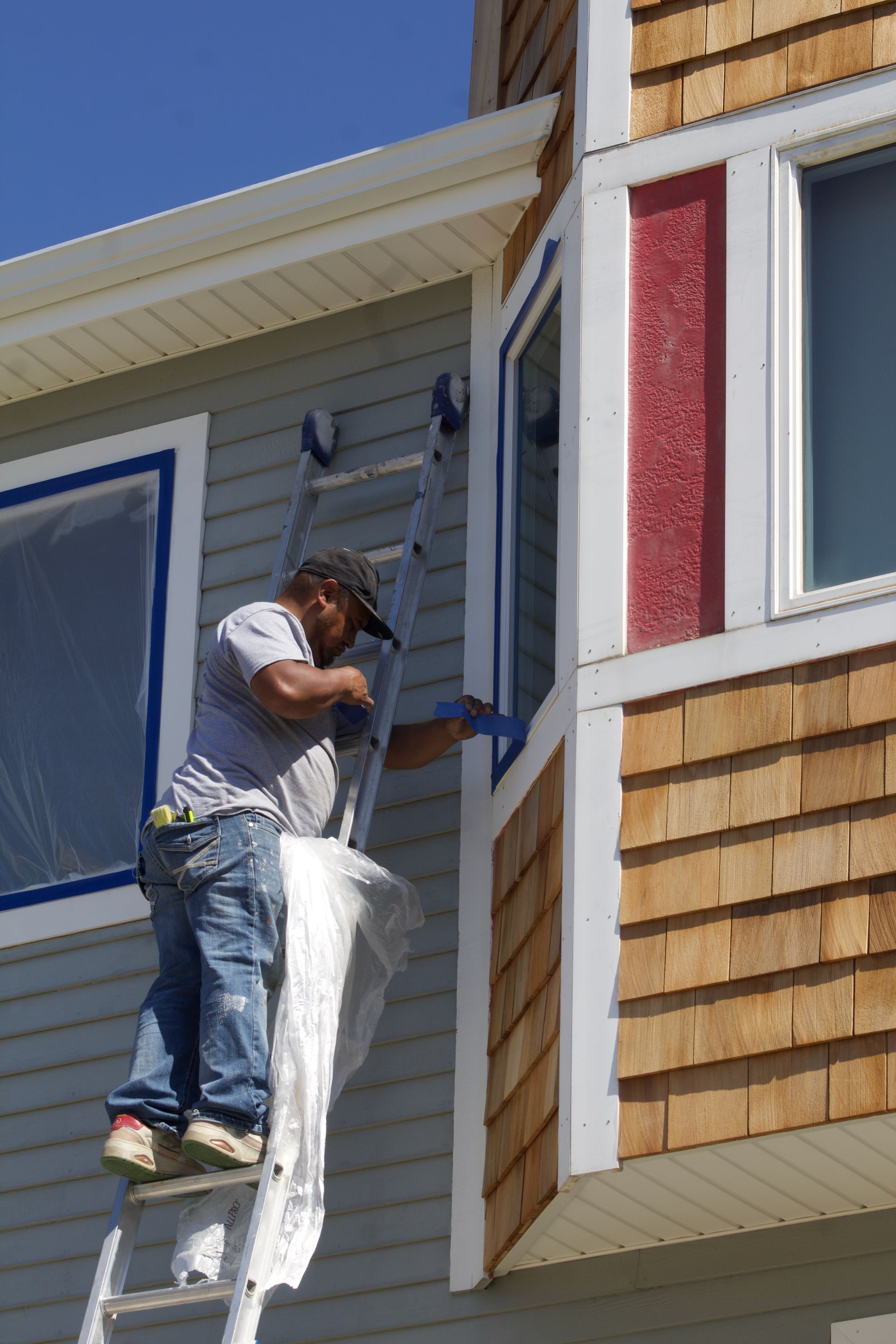 Worker painting the exterior trim of a house while standing on a ladder