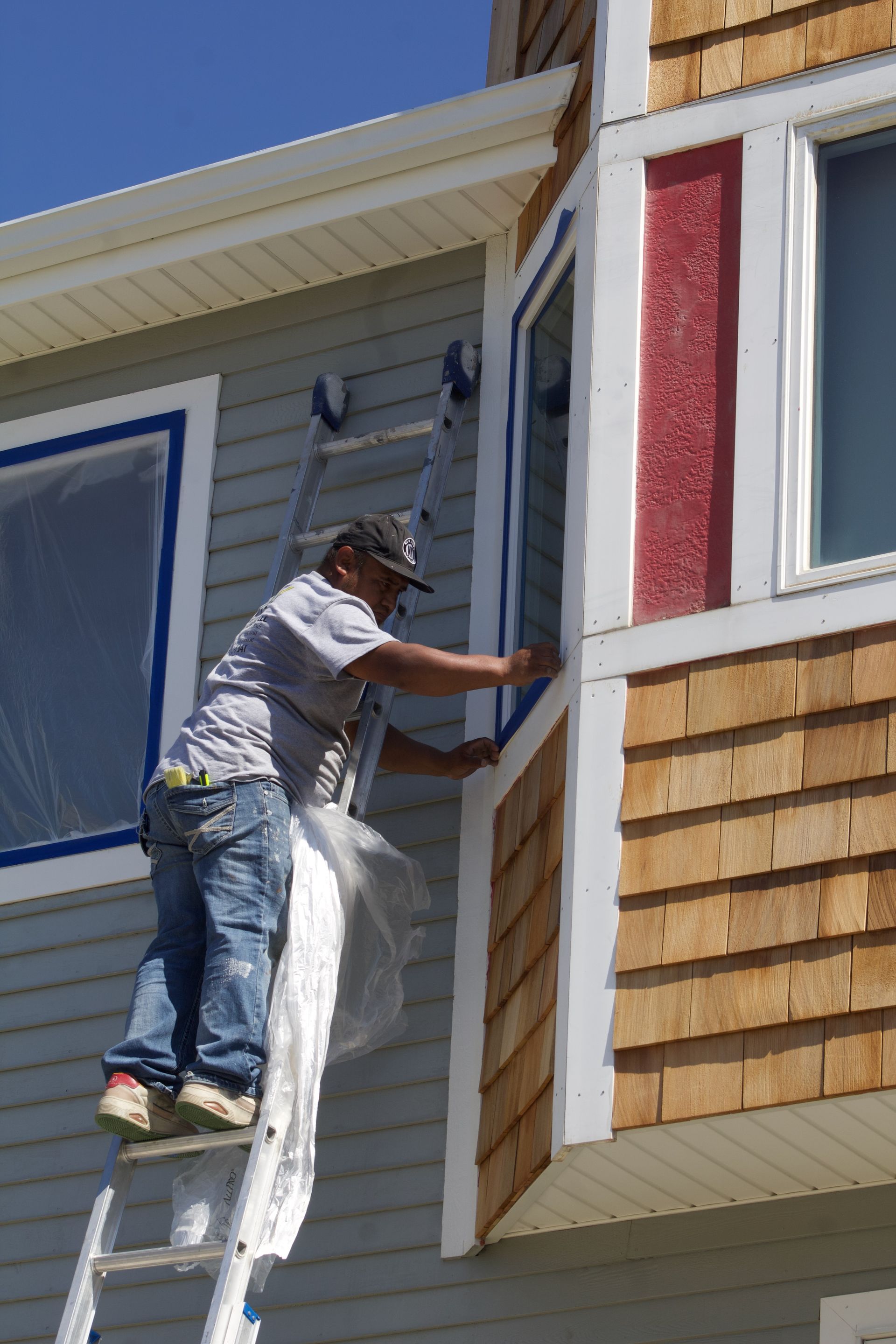 Worker on a ladder painting the exterior trim of a house on the second story