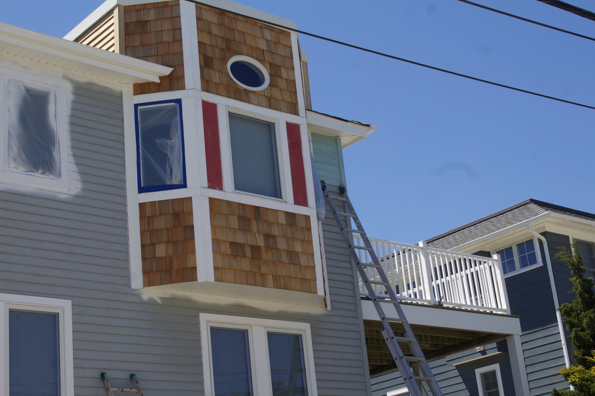House exterior with bay windows and a ladder leaning against the roof on a sunny day