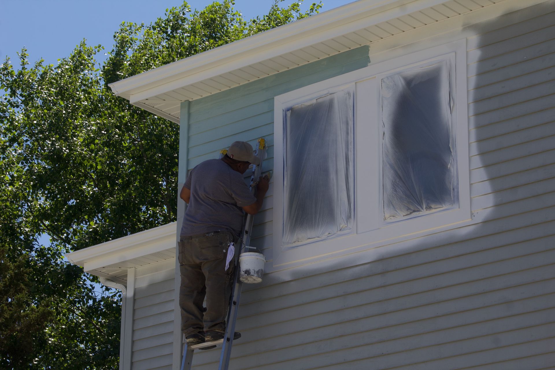 Painter on a ladder painting the exterior of a house beside a window