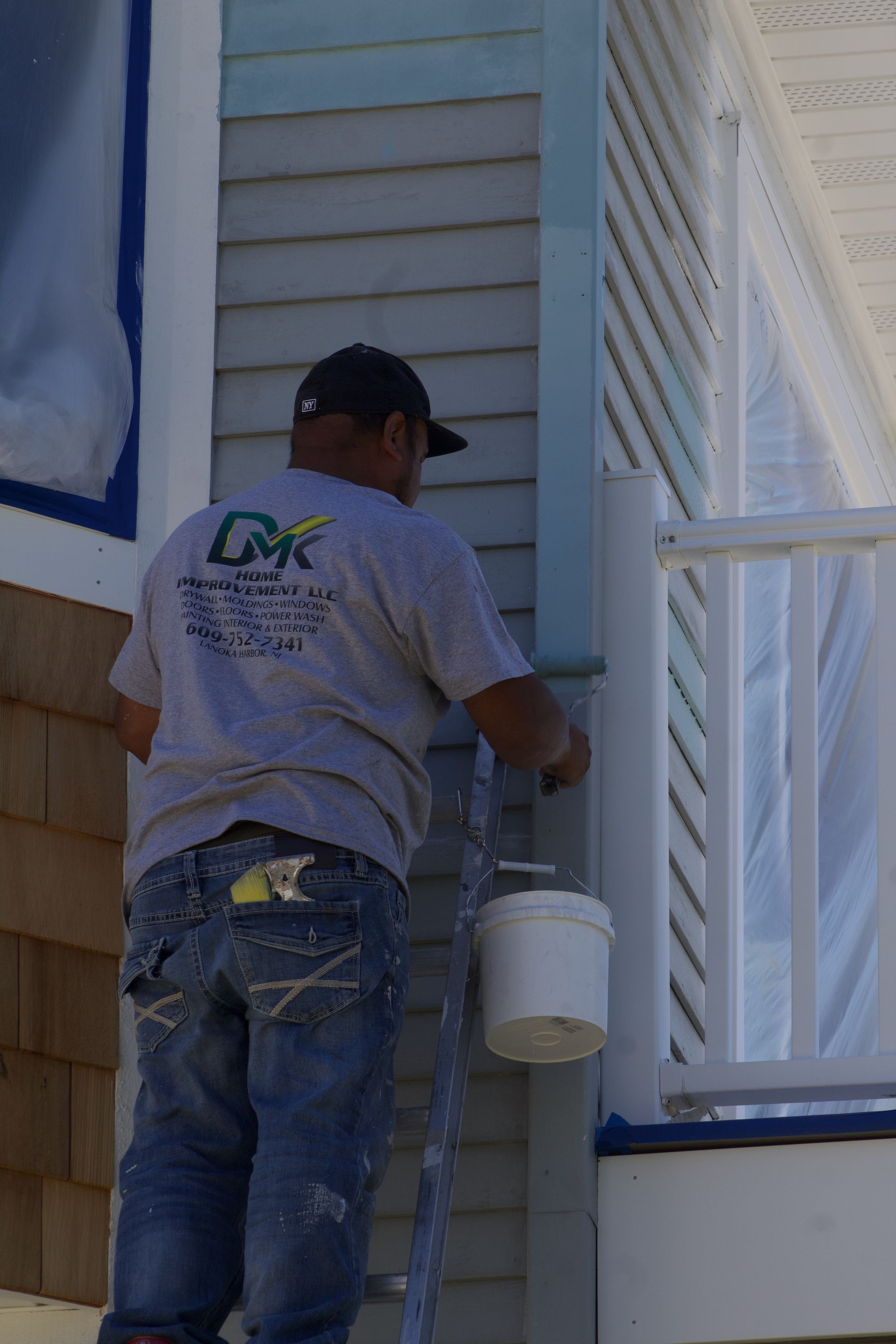 Worker painting the exterior siding of a house while standing on a porch.