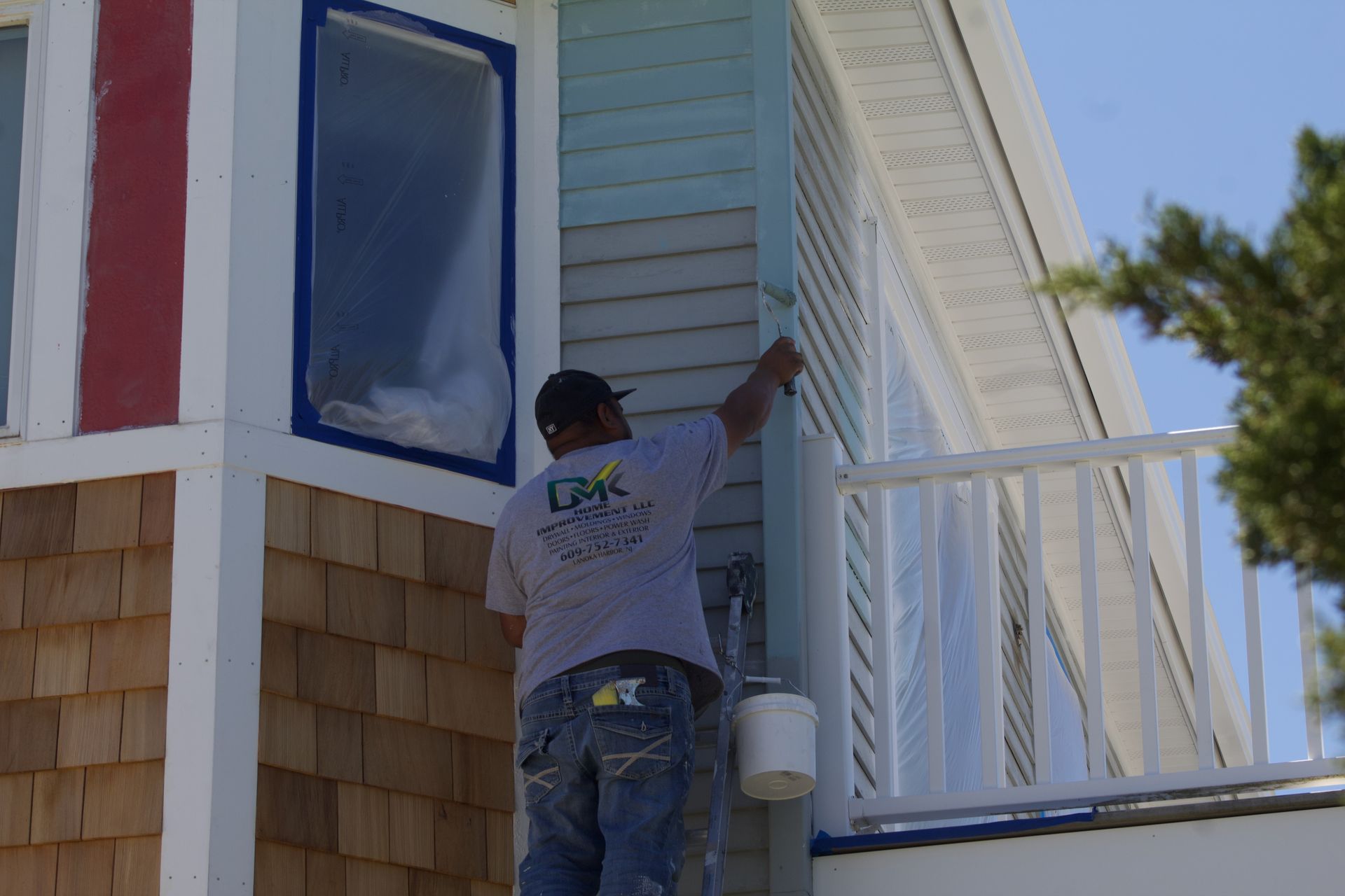 Worker painting the exterior of a light blue house near white trim and a porch railing