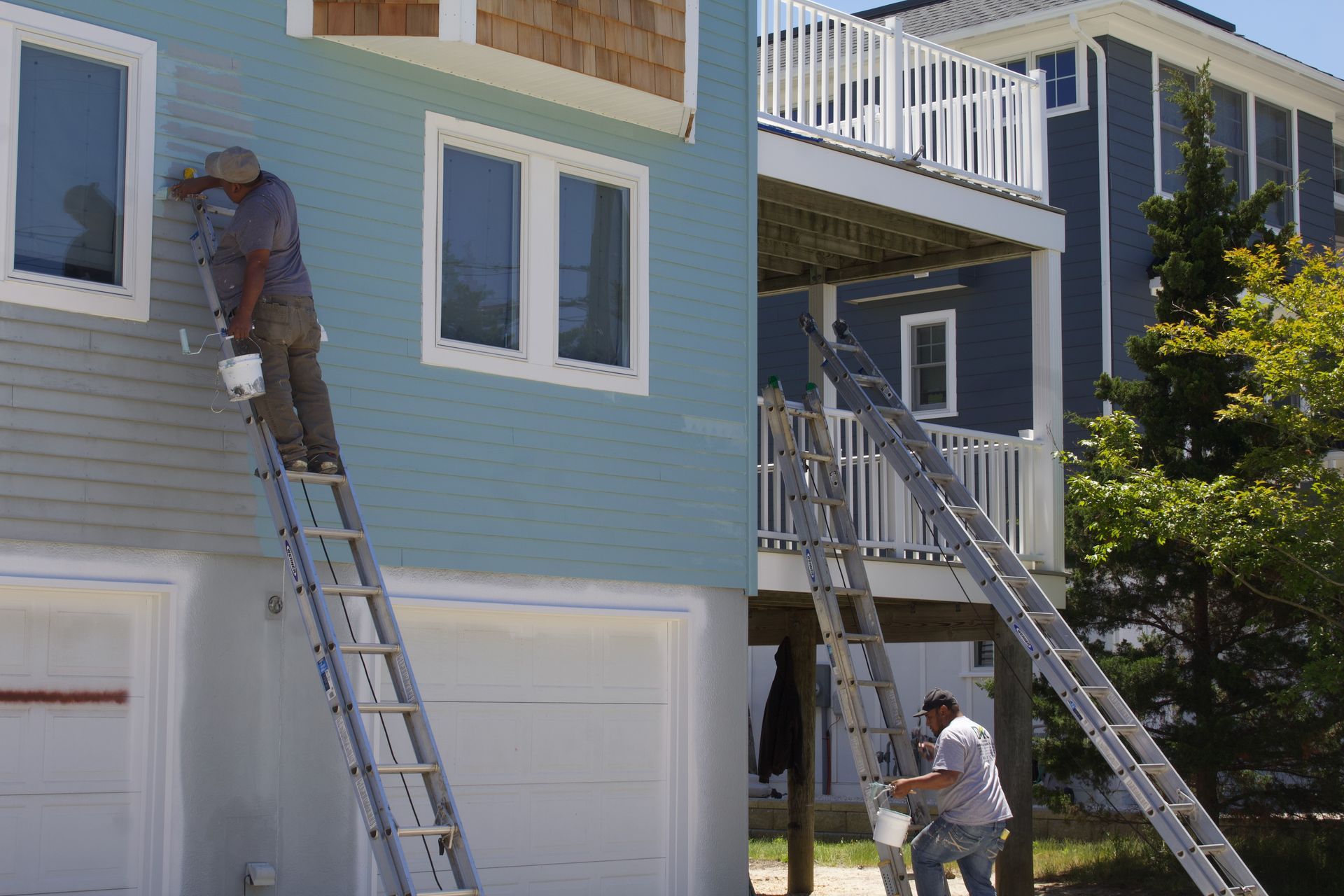 Workers on ladders painting the exterior of a blue house with white trim