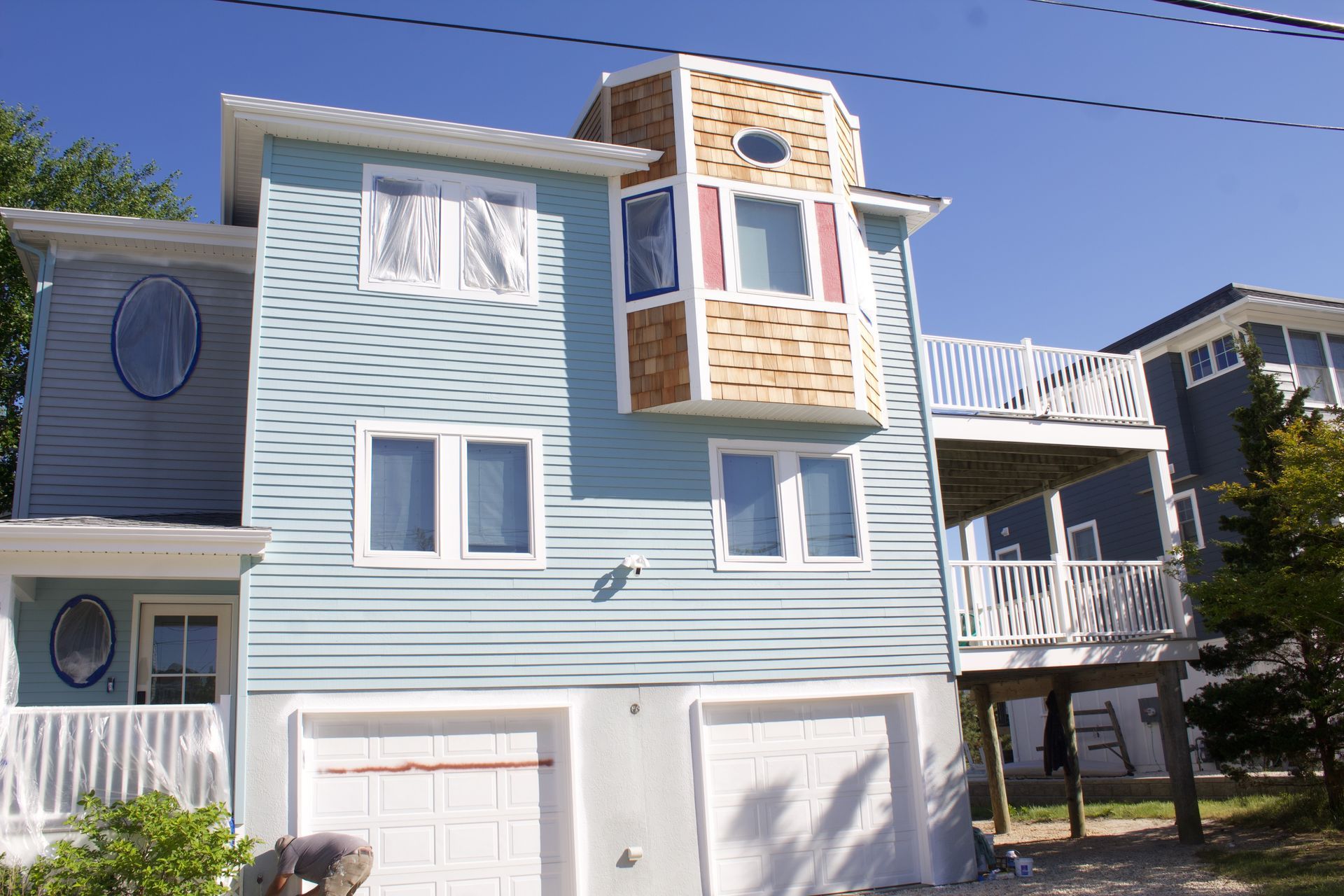 Light blue townhouse with white trim, garage doors, and a small balcony under a clear sky