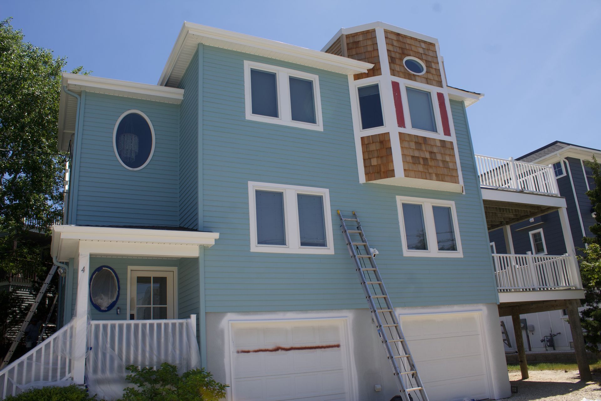 Blue coastal house with white trim, garage doors, and a ladder leaning up to the second floor