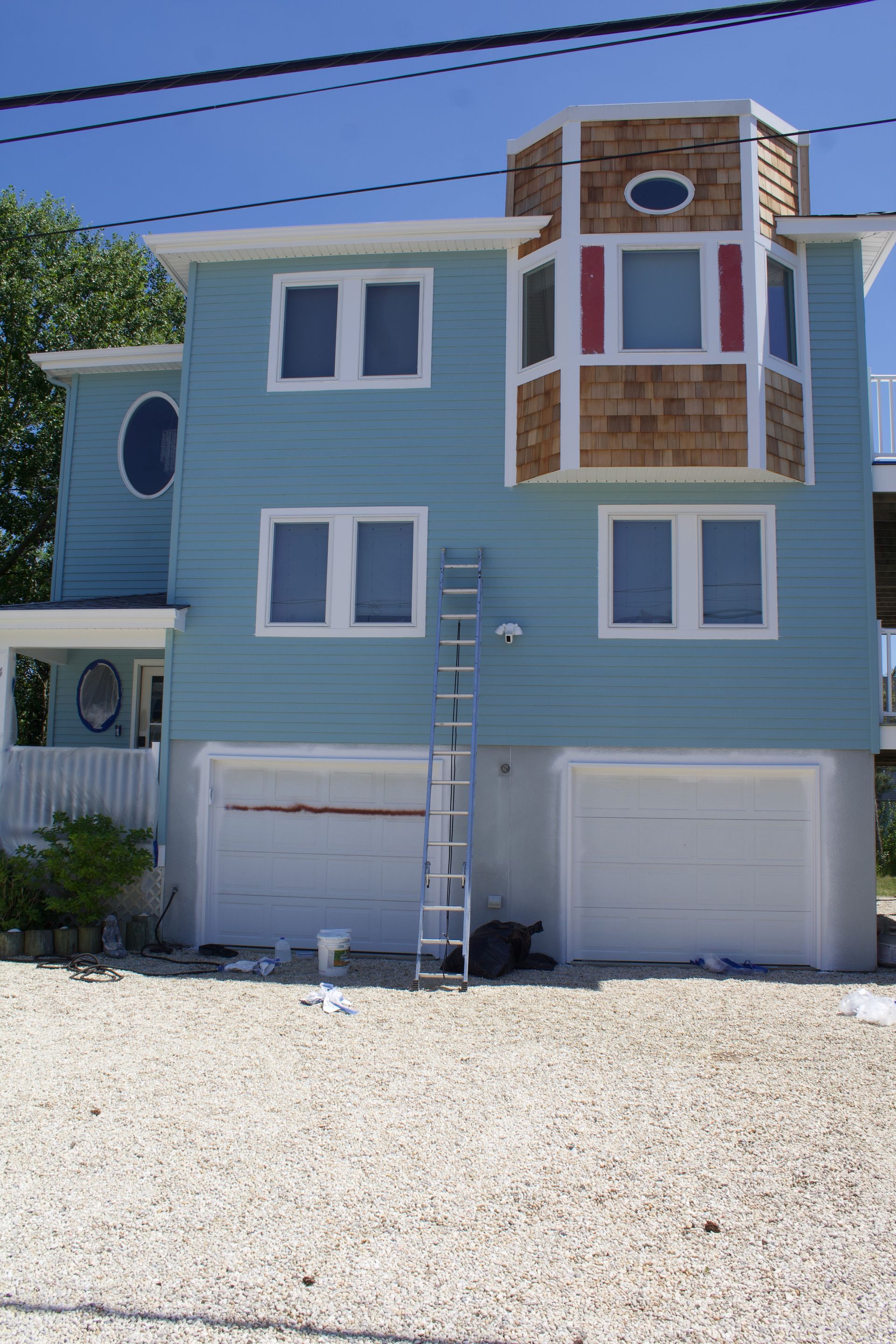 Blue three-story house with white trim, balconies, and a ladder leaning against the front above two garage doors.