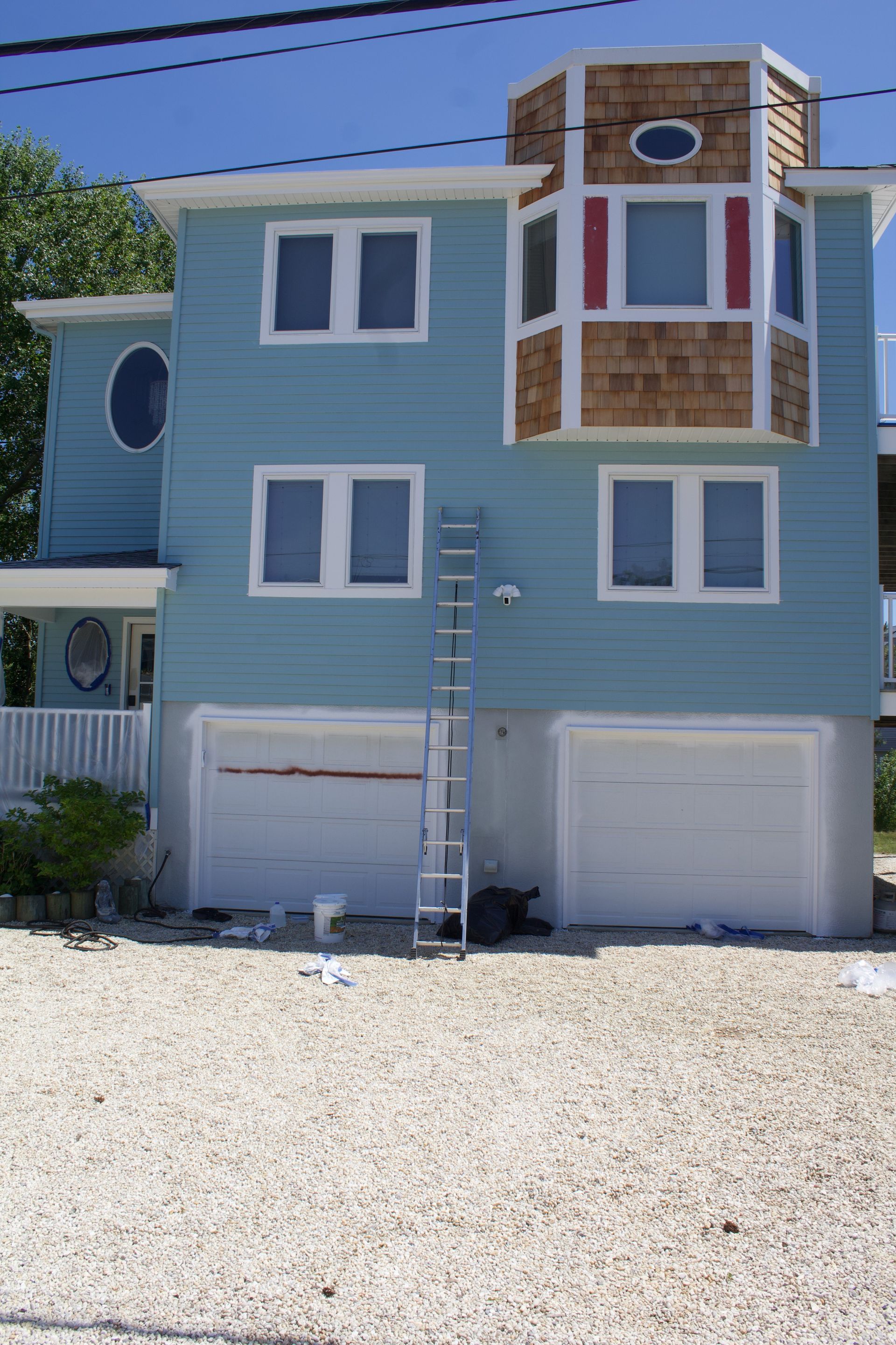Blue beach house with white trim, two garage doors, and a ladder leaning against the front.
