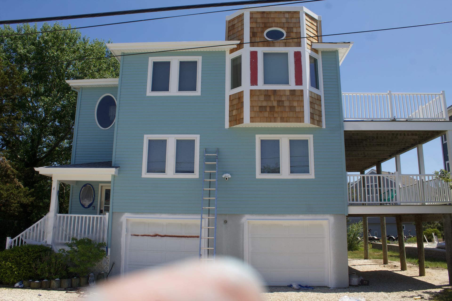 Blue coastal house with white trim, balconies, and garage doors under a sunny sky