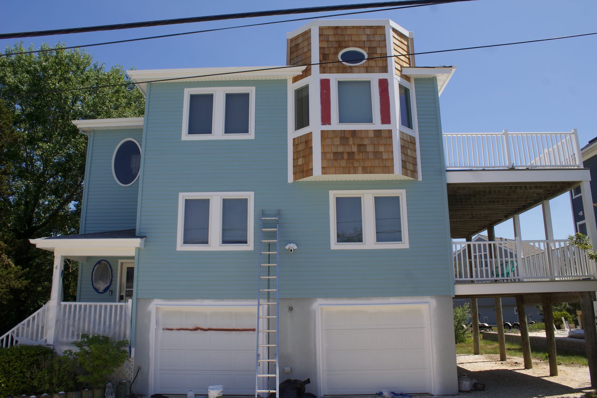 Blue three-story house with white trim, balconies, and a garage under a clear sky
