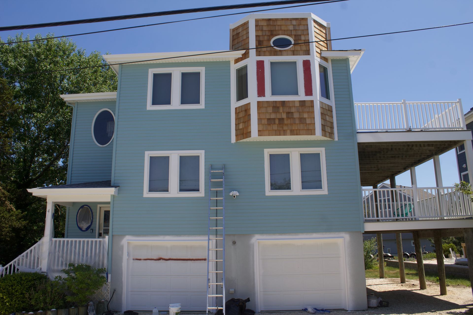 Blue seaside house with white trim, bay window, garage doors, and an elevated deck under a clear sky