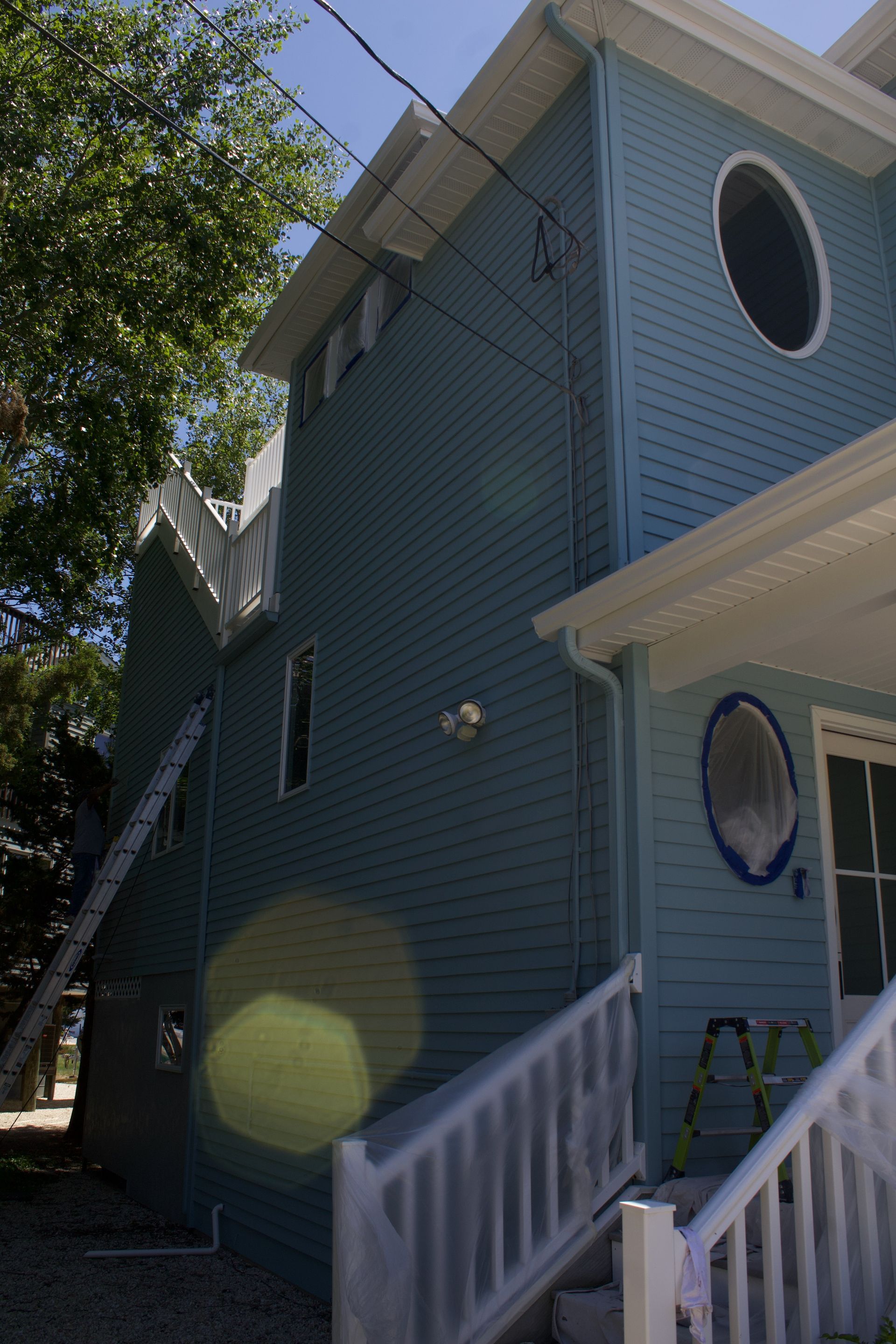 Blue house exterior with white trim, oval windows, and front steps shaded by a tree