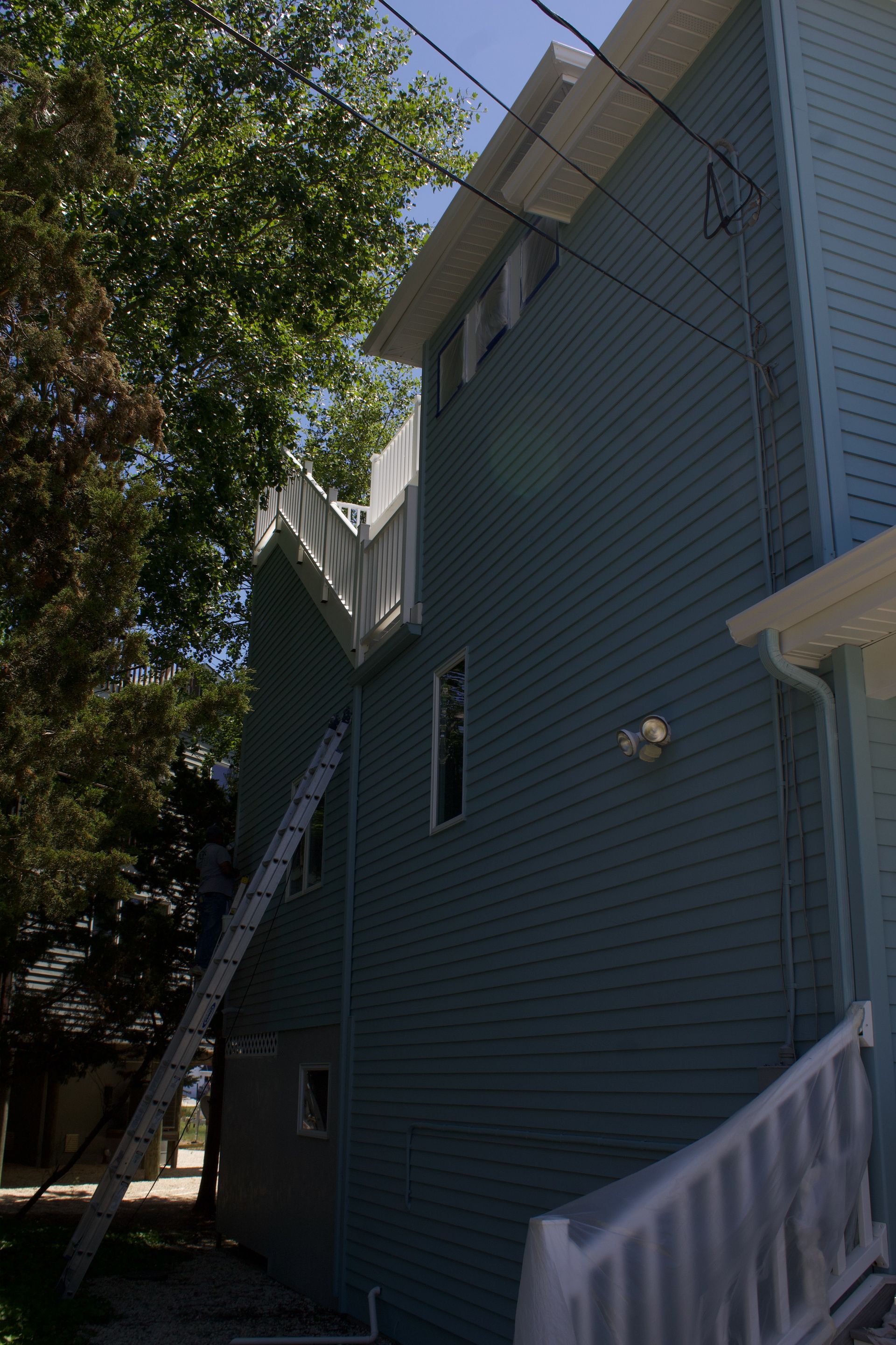 Blue house exterior with steep roof, white trim, and trees beside a narrow side yard