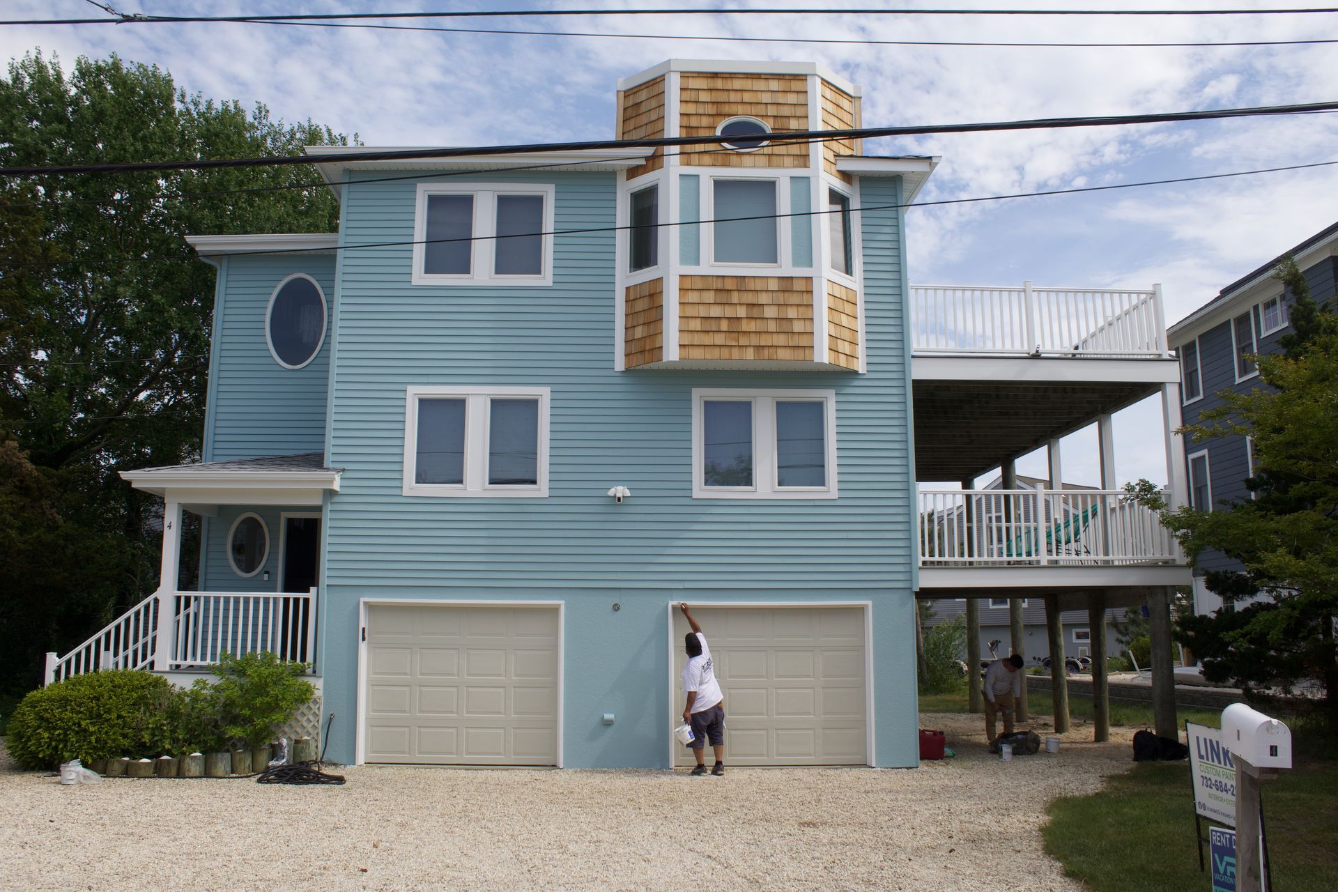 Blue beach house with a person standing in front and a garage below, viewed from the street