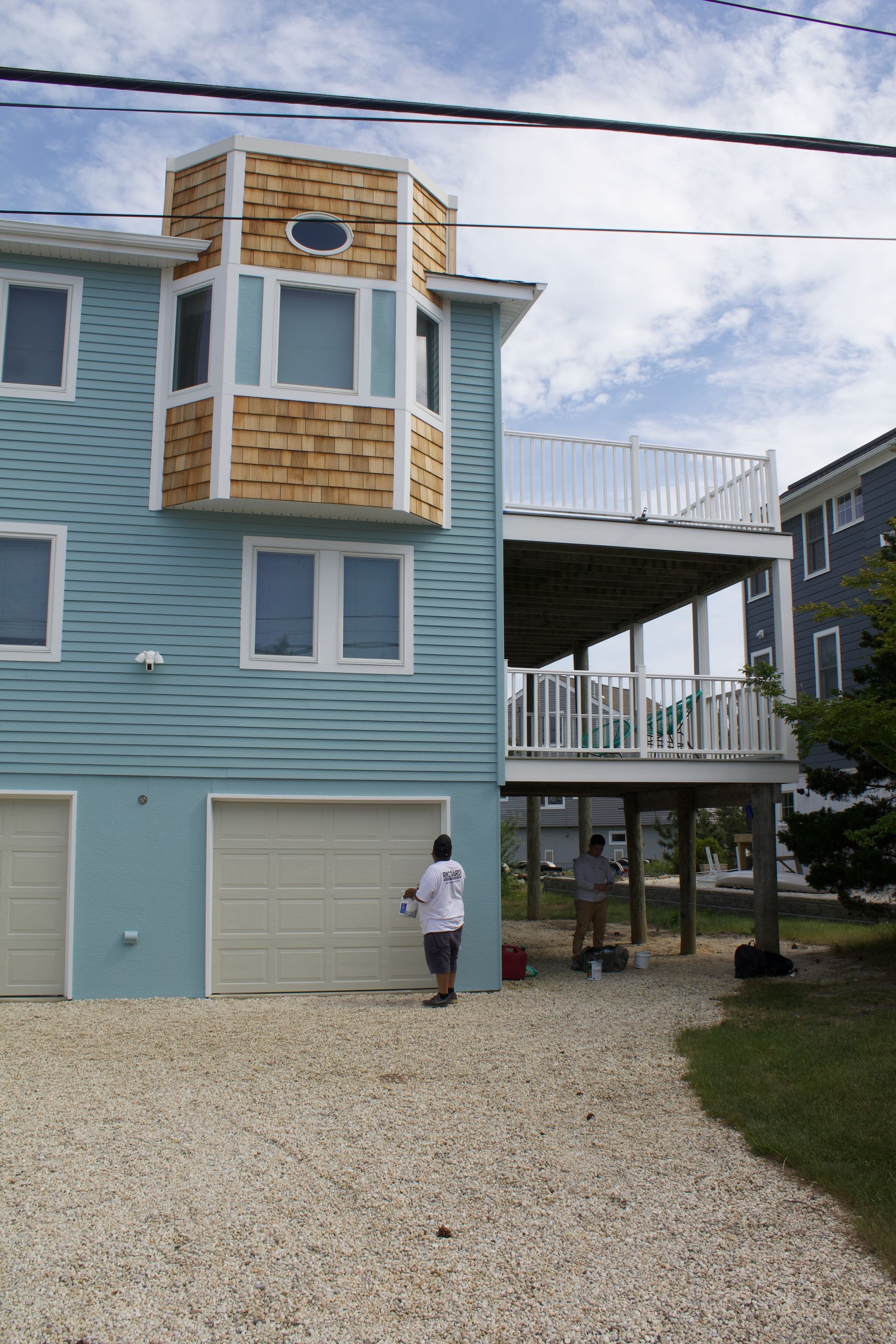 Blue beach house with white balconies and a person standing on the gravel driveway