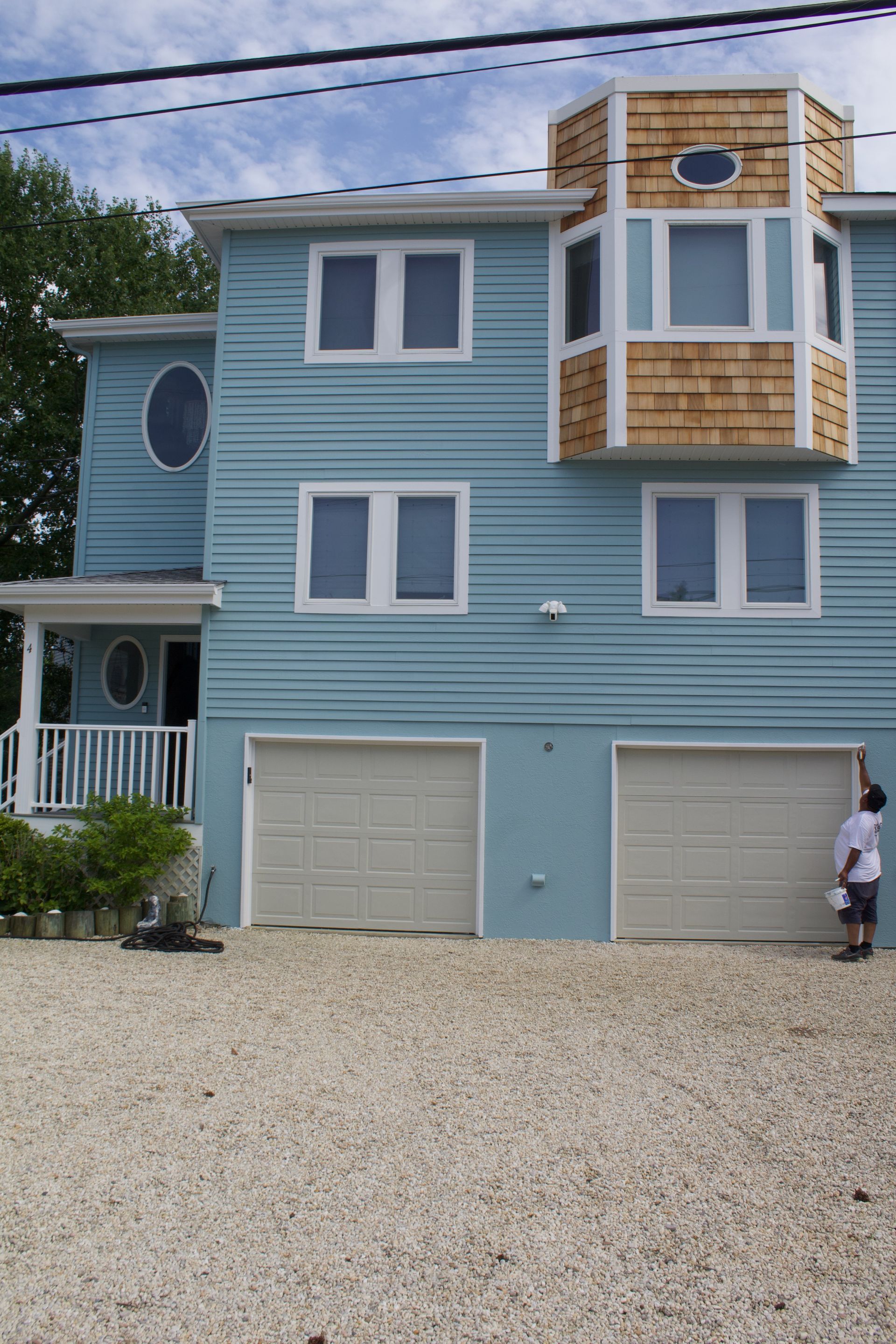 Blue beach house with gravel driveway, garage doors, and a person standing near the right side