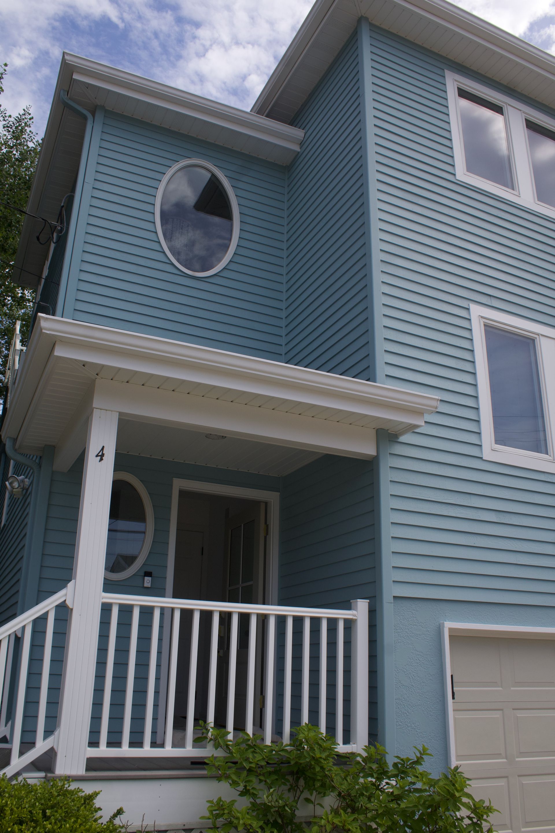 Blue two-story house with white trim, round window, and small front porch and garage.