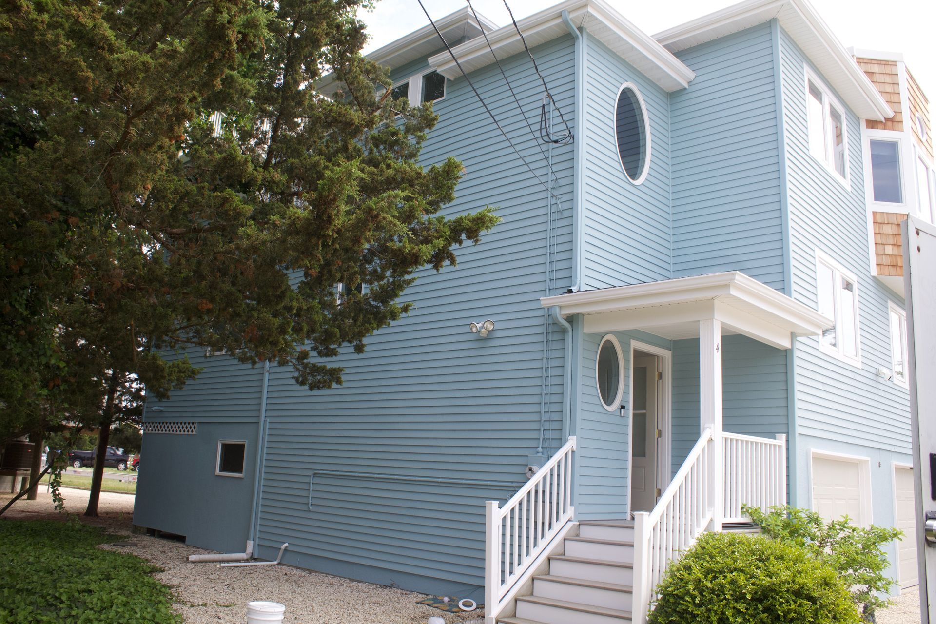Blue two-story house with white trim, stairs, and a tree in front