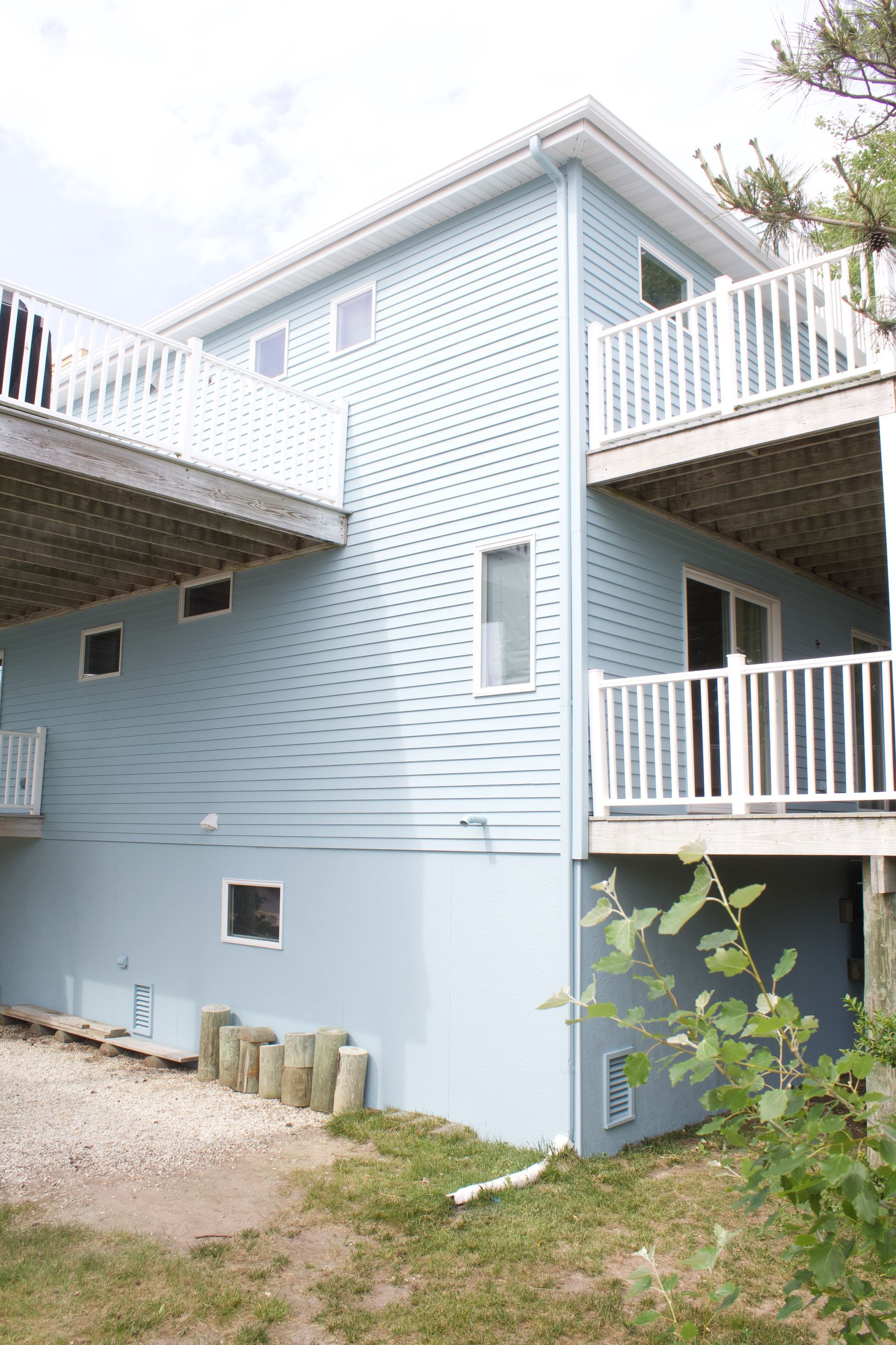 Light blue house exterior with white balconies and stairs, seen from a side yard