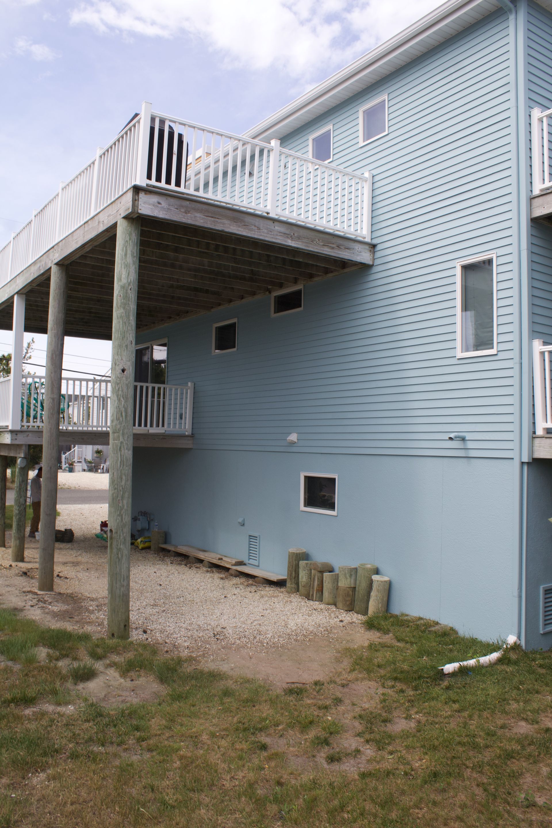 Blue-gray building with raised deck and stairs, seen from the ground with grass and gravel below