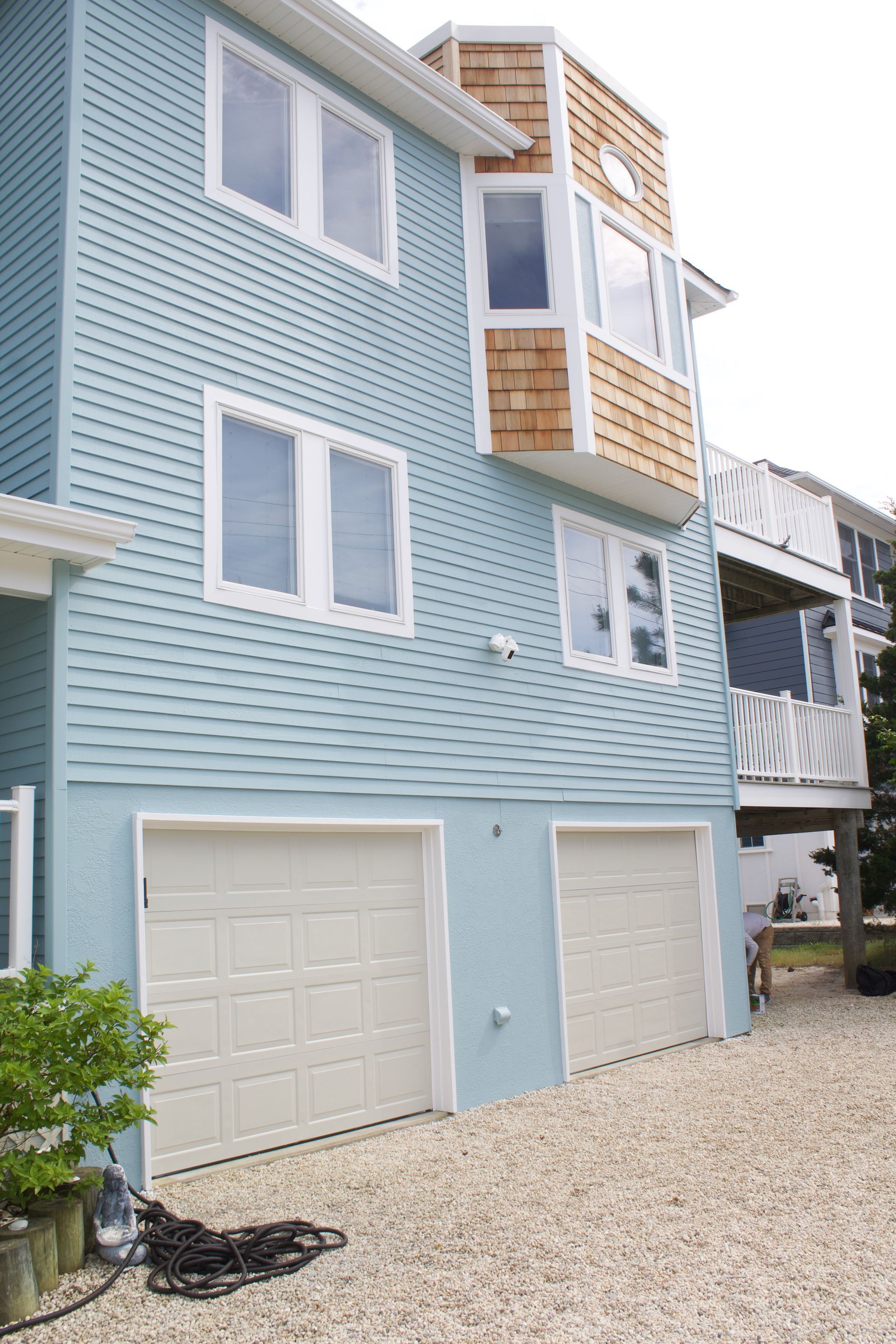 Light blue beachfront condo with balconies and two garage doors on a gravel driveway