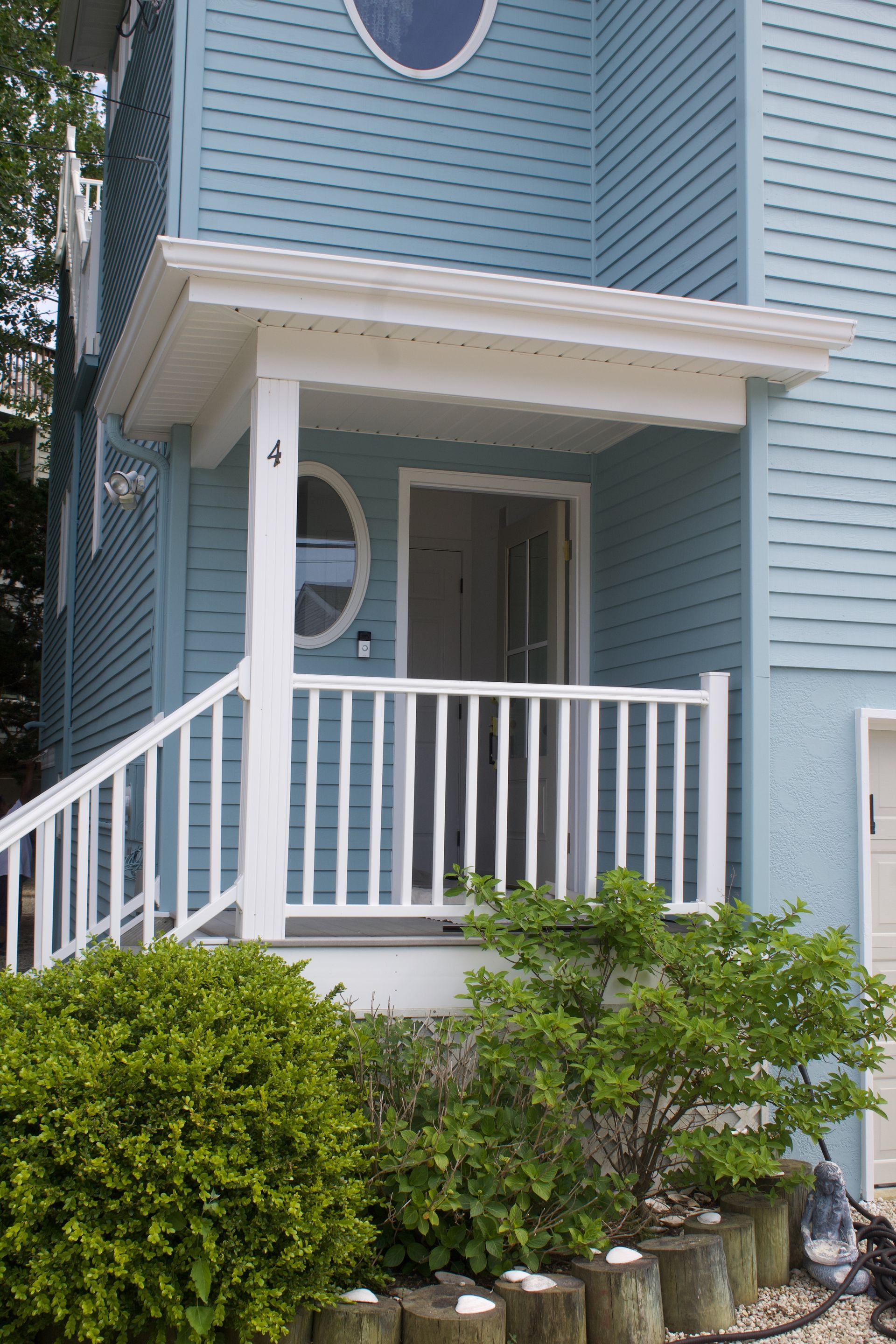 Blue townhouse entry with white porch railing, front steps, and shrubs in front