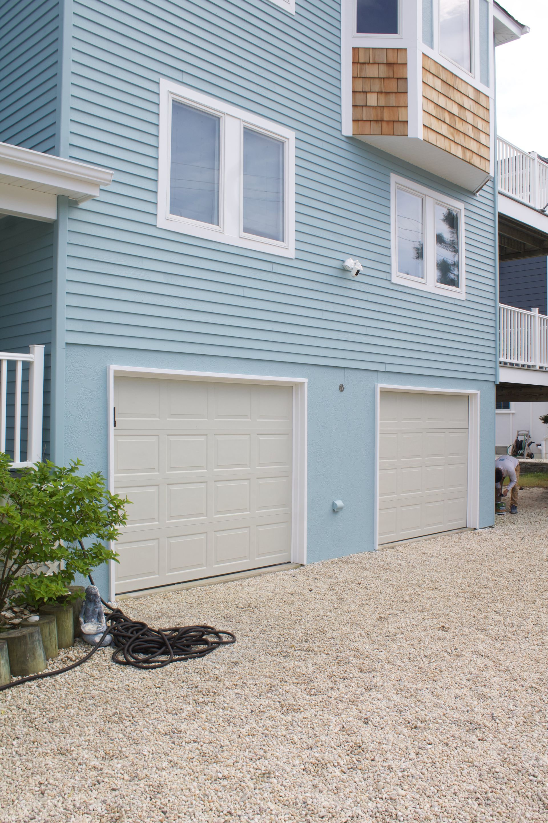 Blue house exterior with two white garage doors and gravel driveway