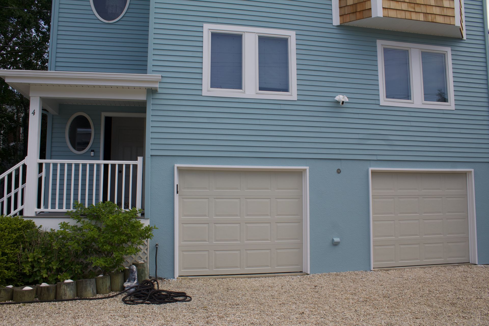 Blue seaside house with white trim, two garage doors, and a small front porch
