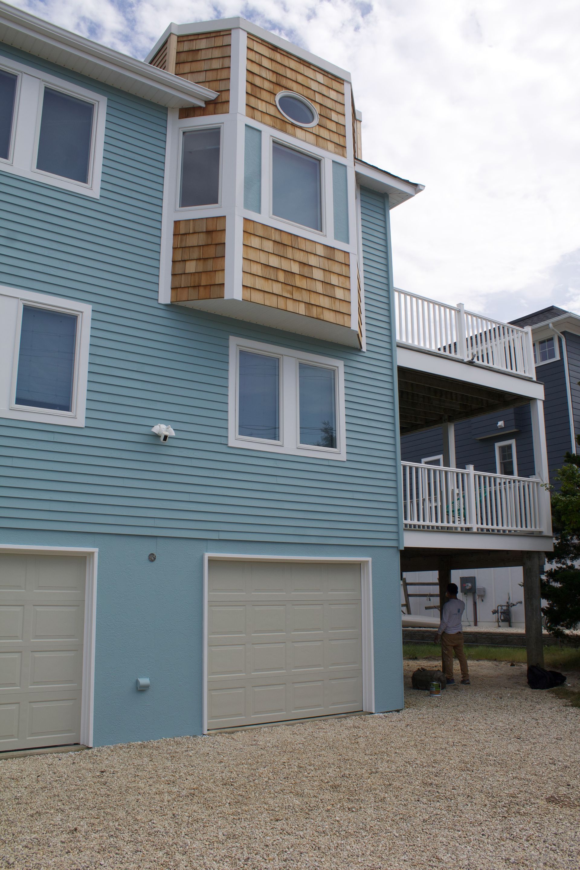 Blue beach house with white trim, balconies, and garage doors on a gravel driveway