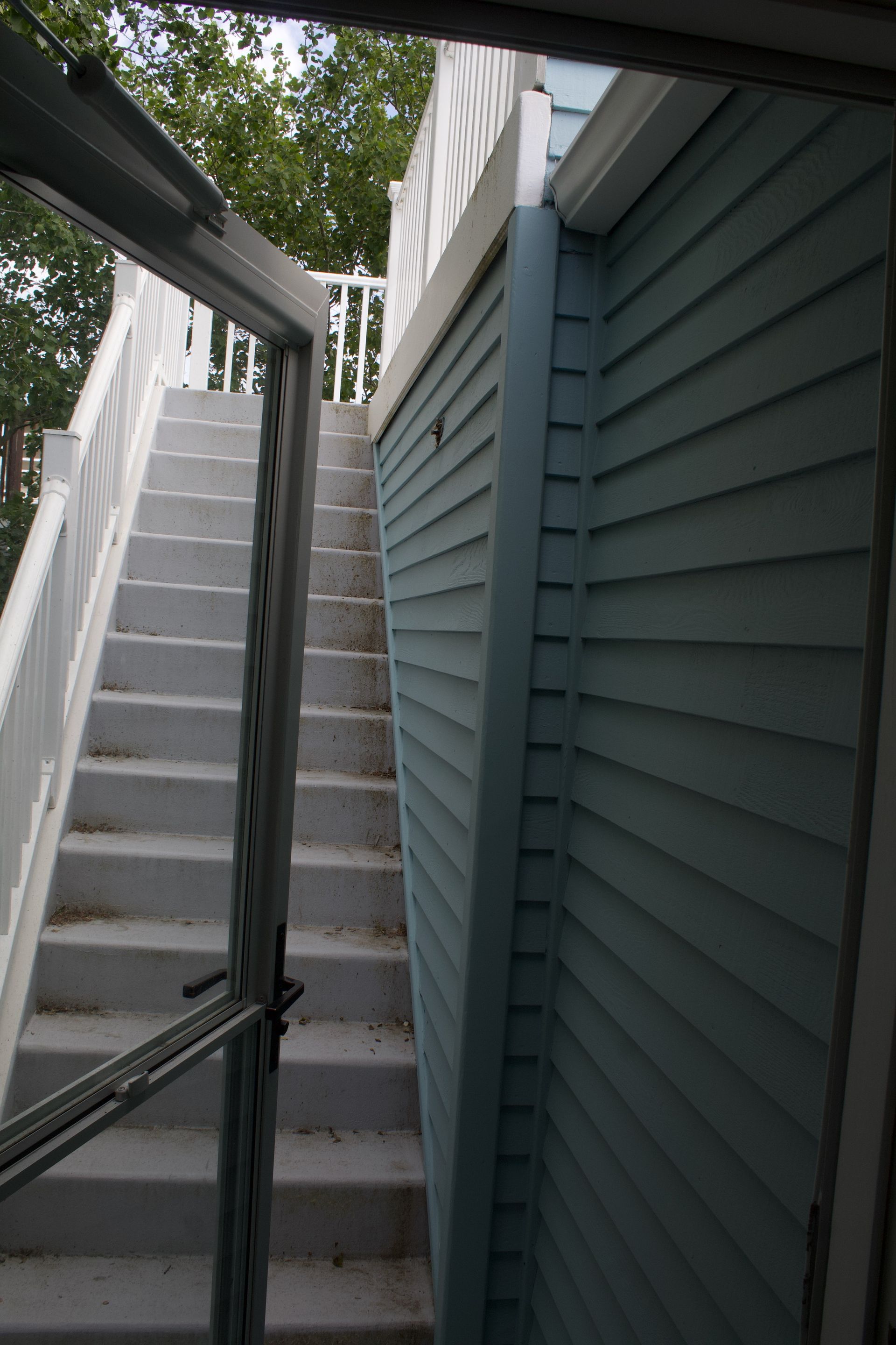 Narrow outdoor stairway beside a teal-sided building, viewed between metal railings.