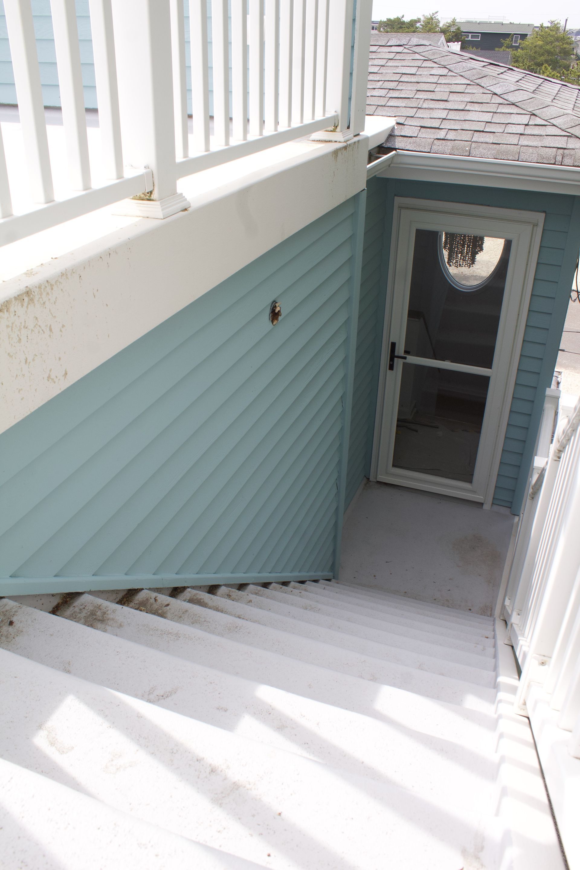 Stairwell beside a teal house exterior with white railings and a small door at the bottom