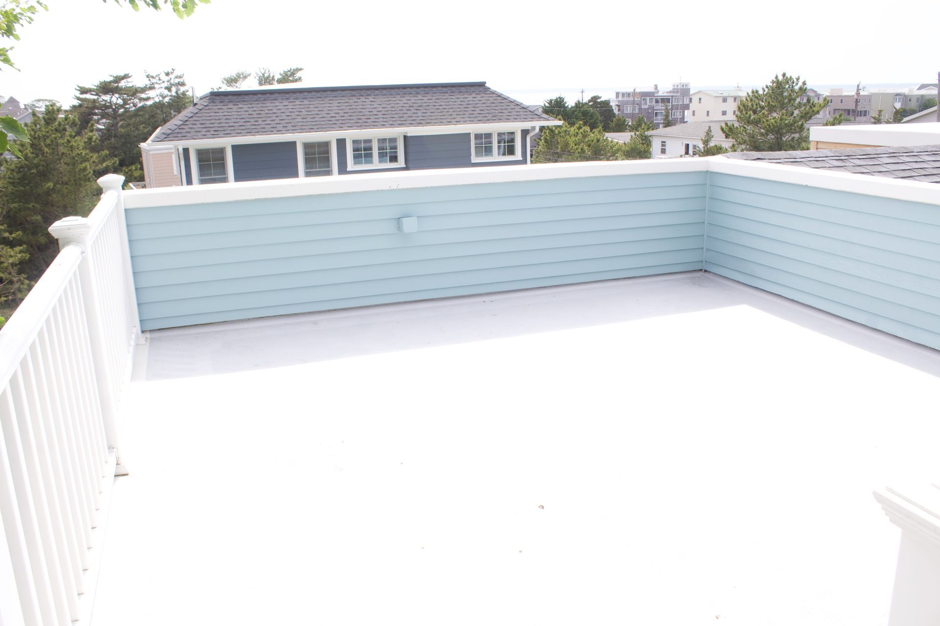 Empty white rooftop deck with pale blue privacy walls and a house view in the background