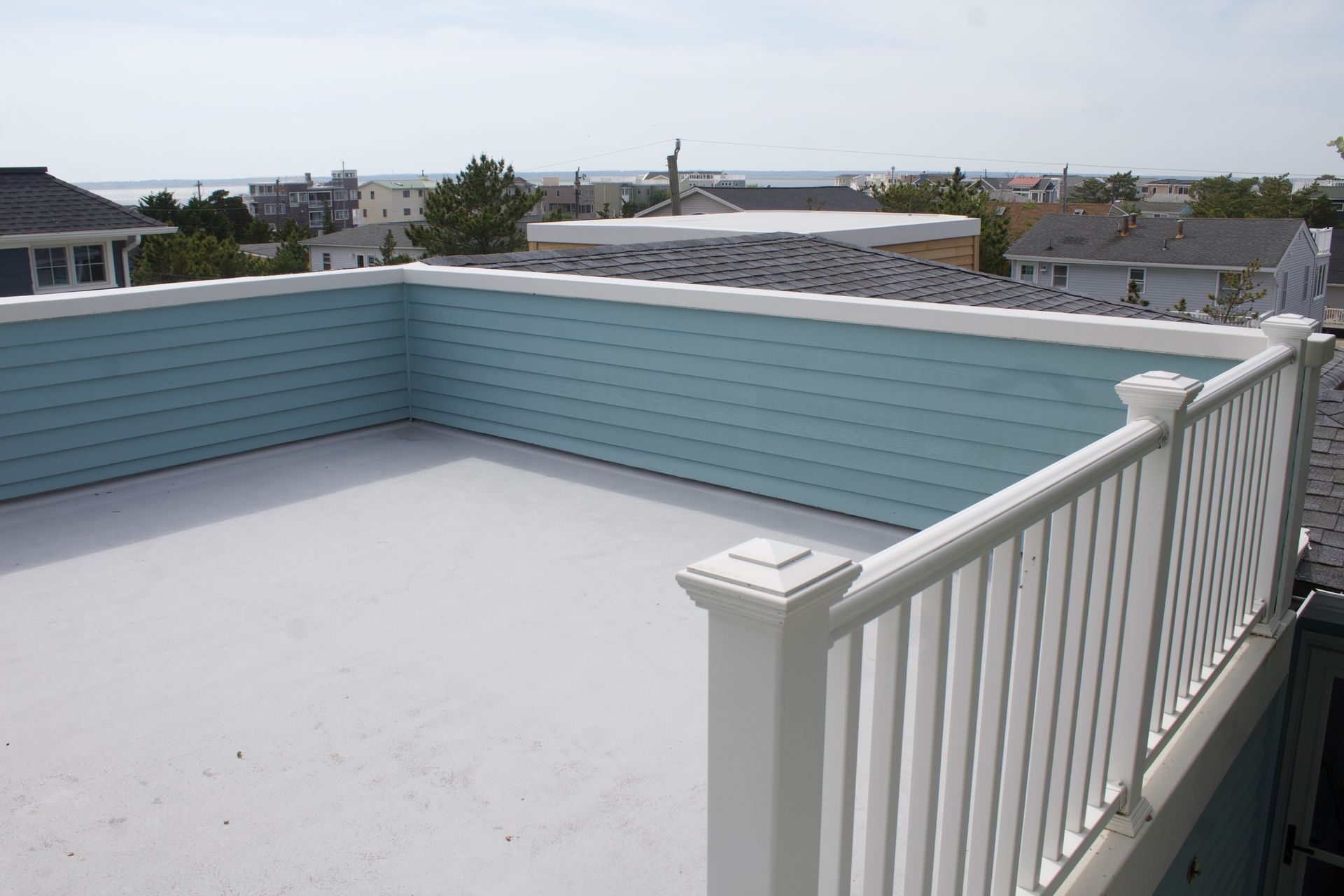 Rooftop deck with white railing and light blue privacy wall overlooking neighborhood homes