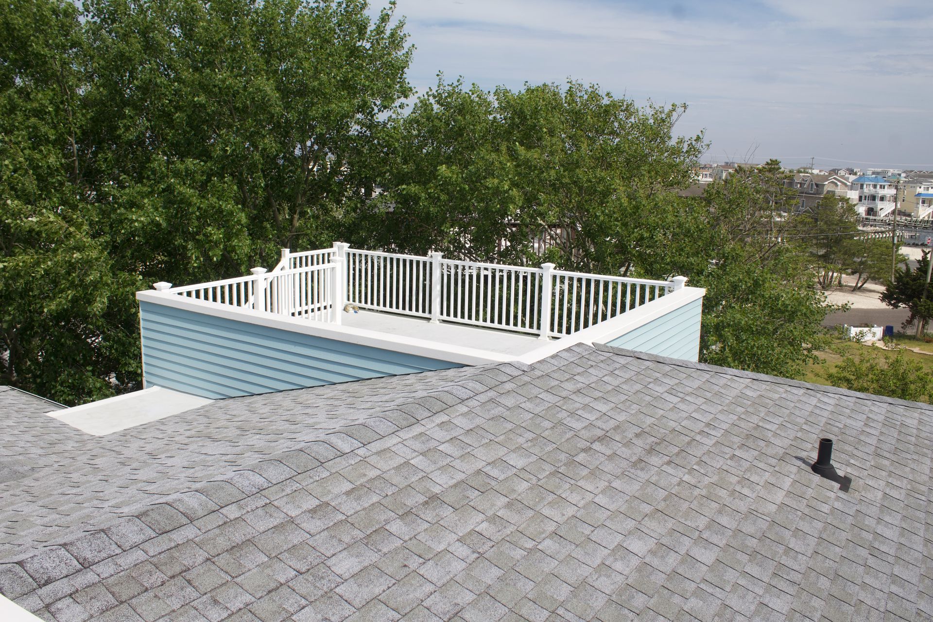 Roof with white railing deck beside trees and distant buildings