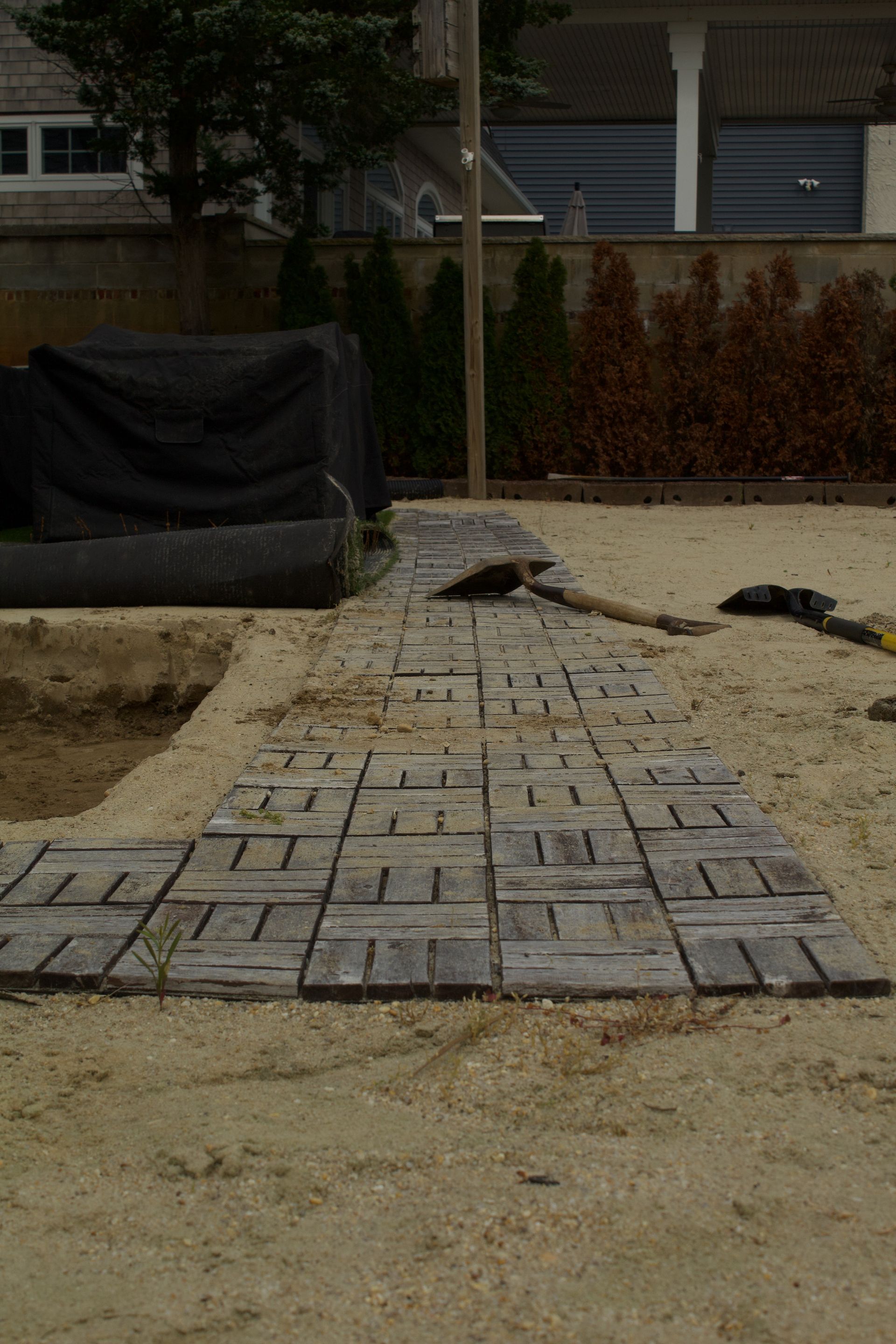 A stone walkway under construction with rectangular pavers on a sandy surface beside a building