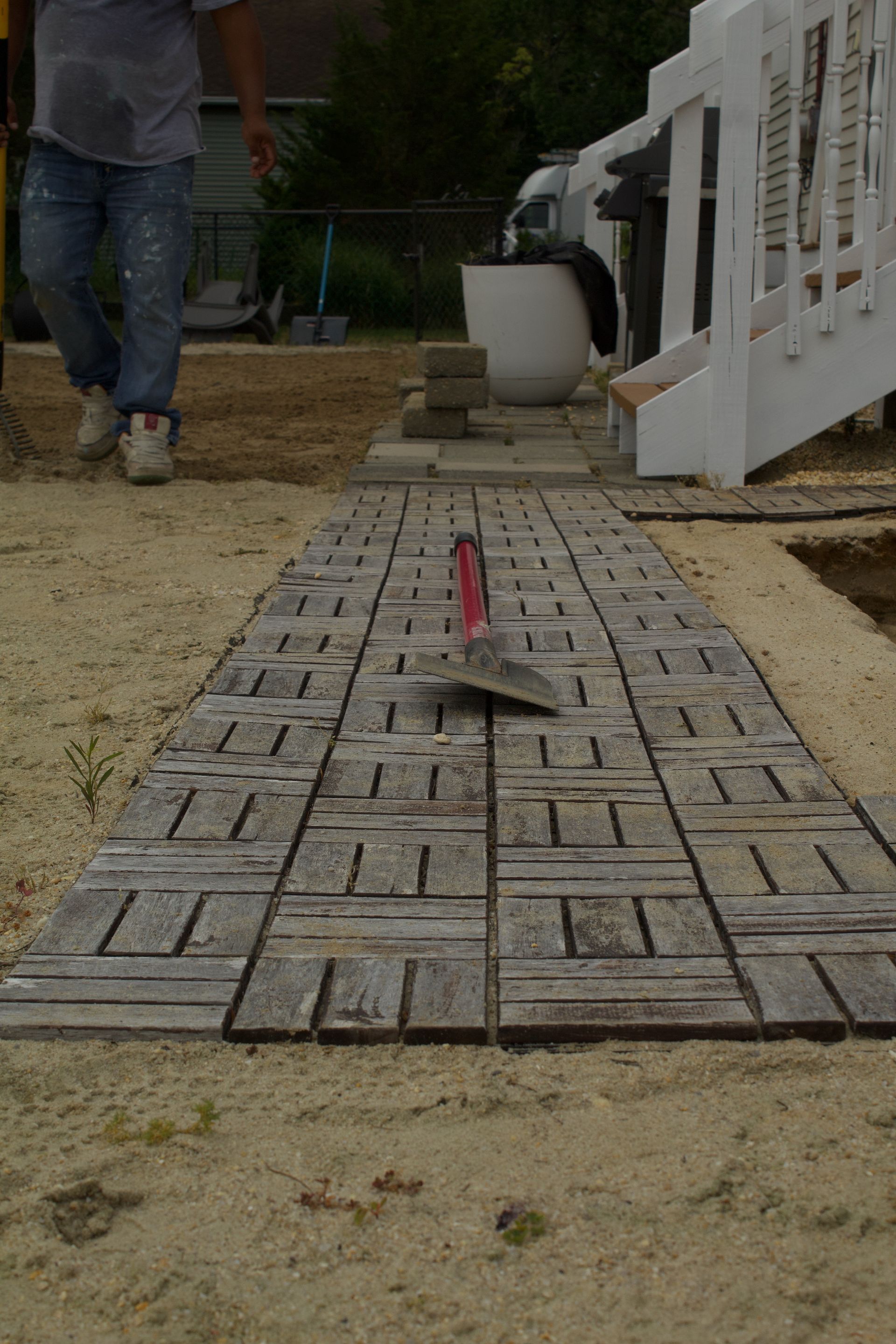A trowel on a gray paver path under construction, with a person standing nearby.