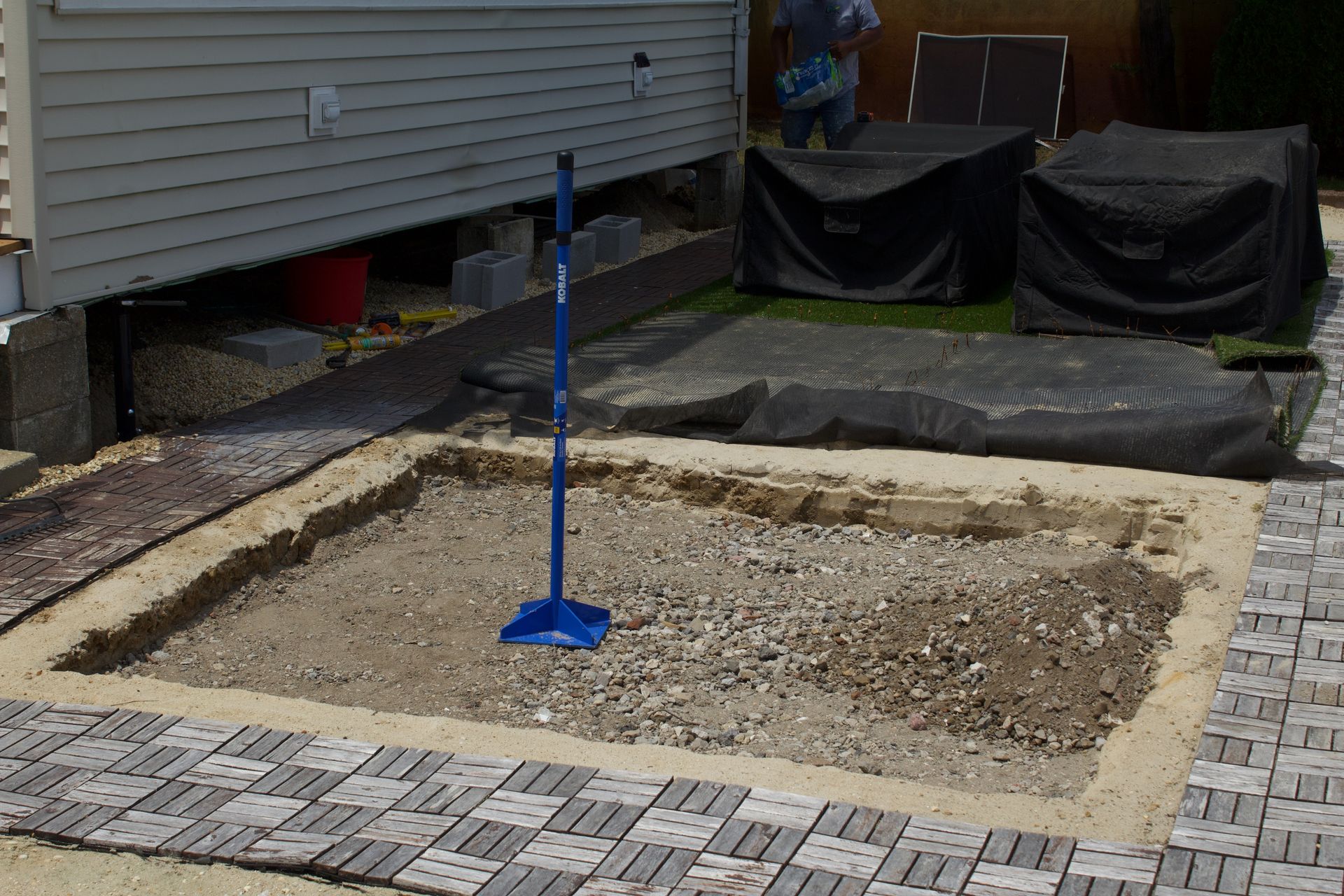 Small backyard patio area with gravel and bordered beds, blue pole centered near a house.