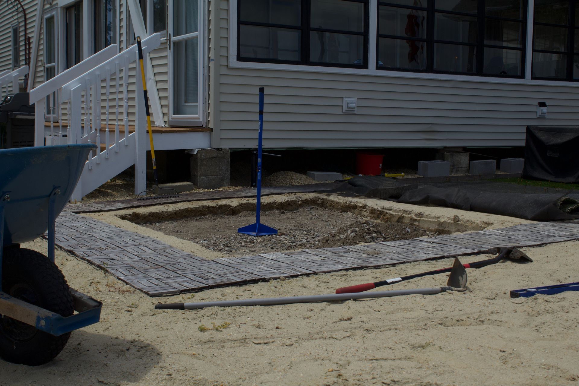 House exterior with a gravel work area, blue pole, and construction tools on the ground.