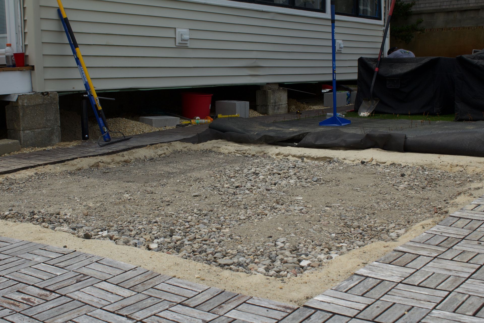 Backyard construction area with a gravel base surrounded by pavers beside a house