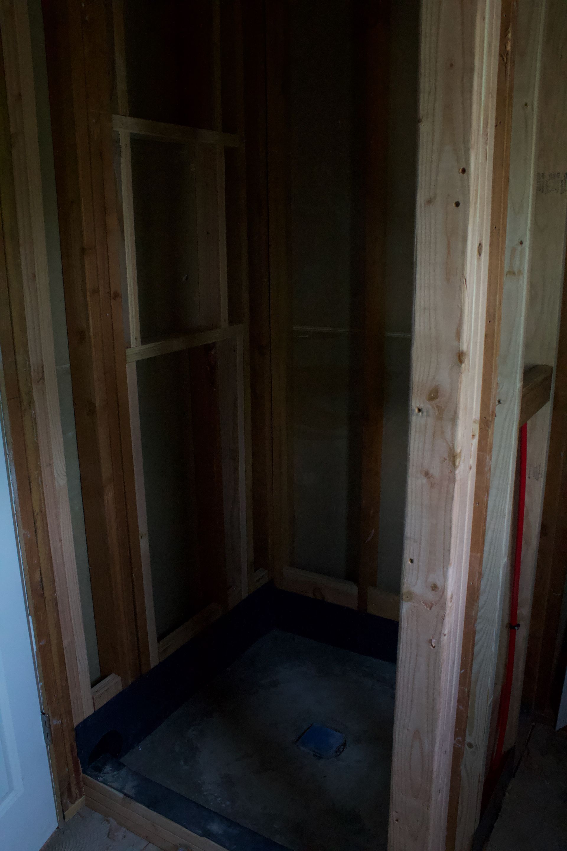 Unfinished wooden shower stall with exposed studs and a dark floor