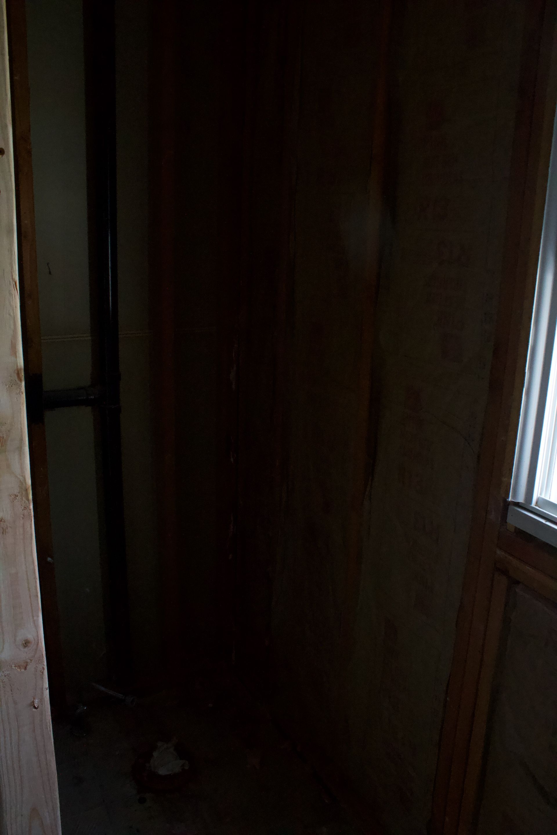 Dim narrow hallway with a dark wooden door and a window on the right