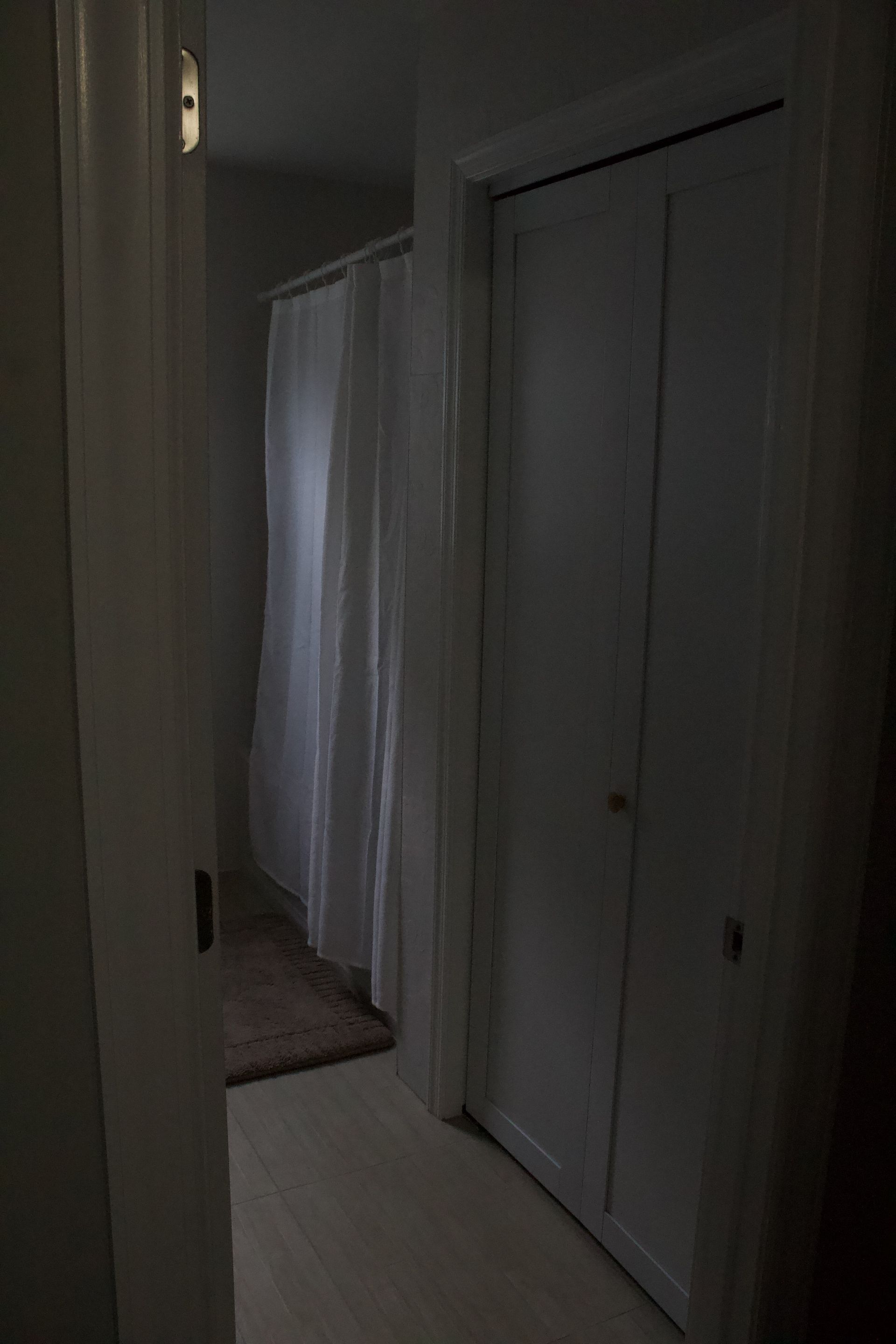 Dim hallway with white closet doors and a white curtain at the far end.