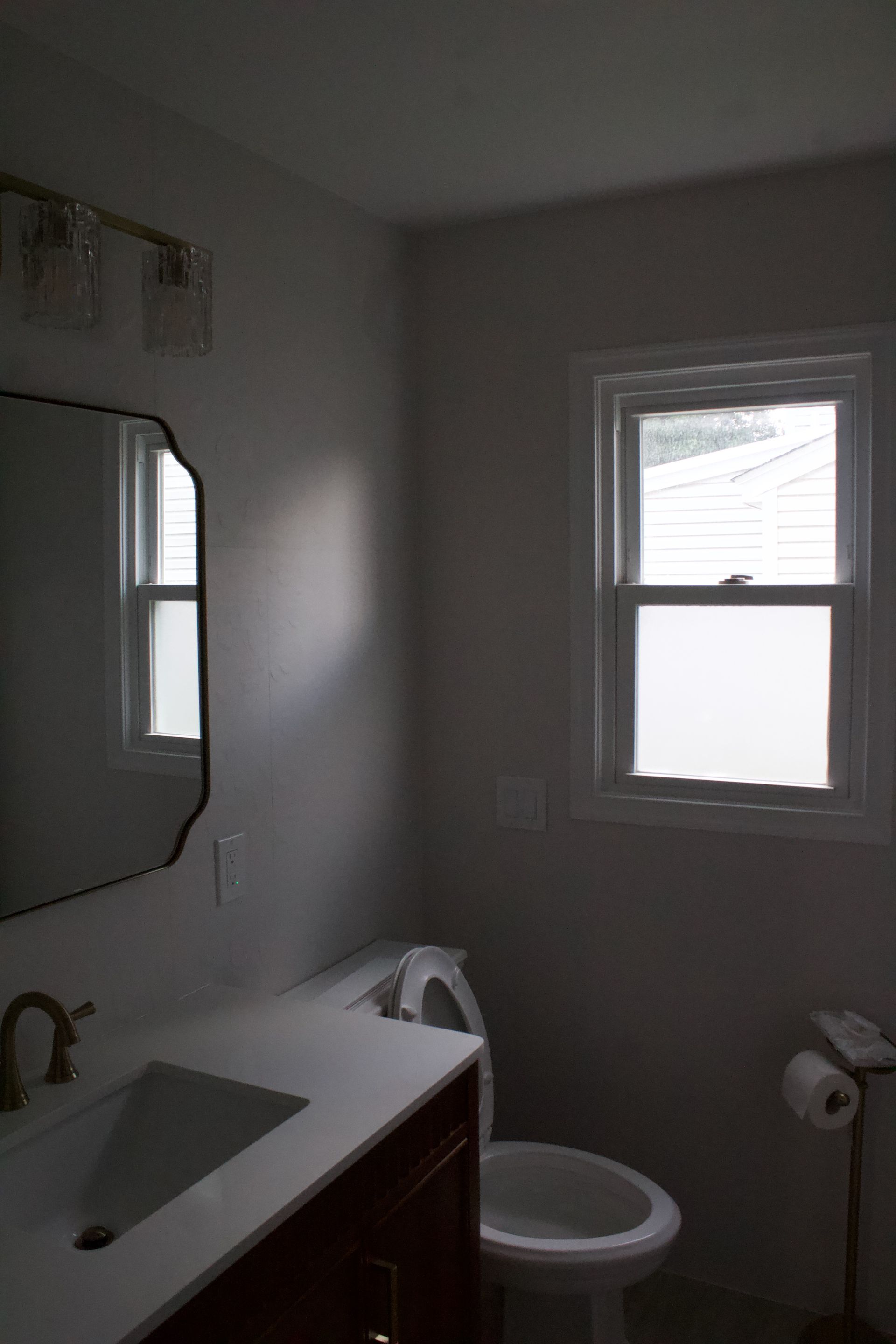 Small bathroom with sink, mirror, toilet, and a window letting in light.