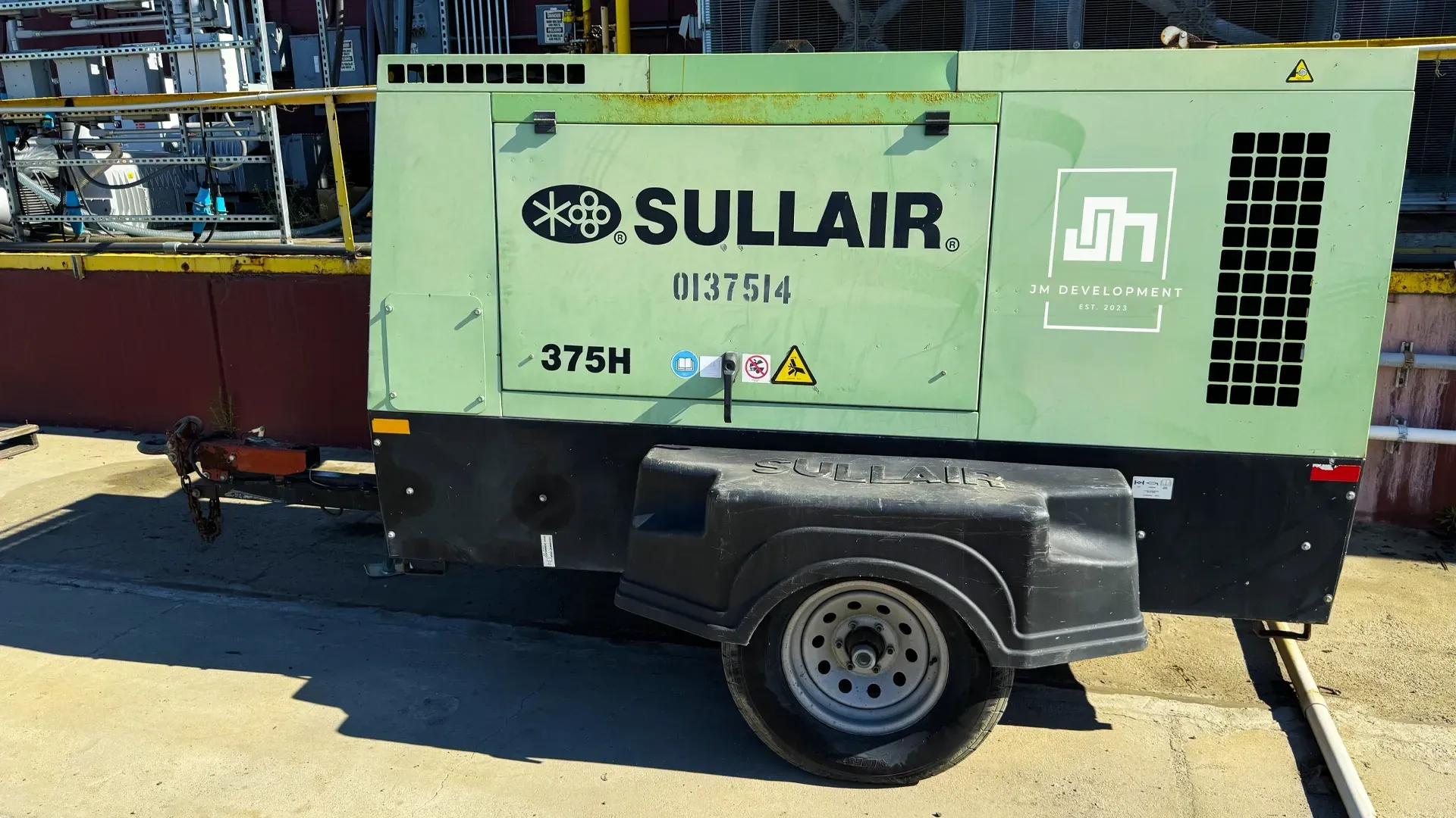 A green industrial Sullair air compressor with JM Development logo on a construction site.