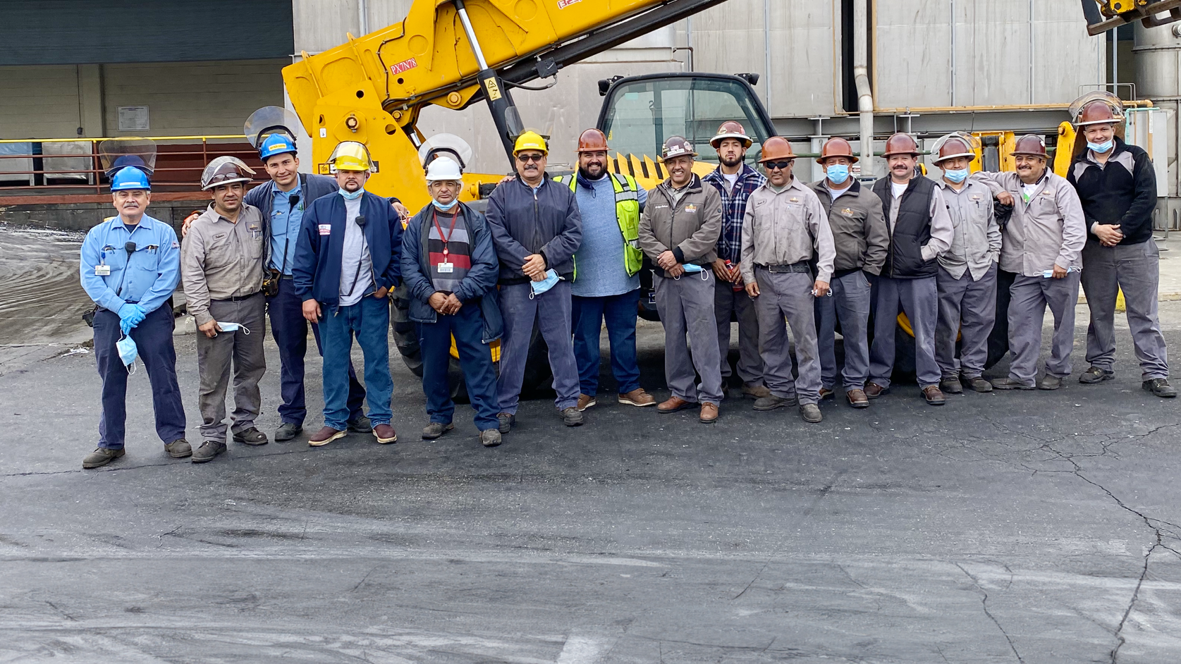 A group of construction workers are posing for a picture in front of a yellow crane.