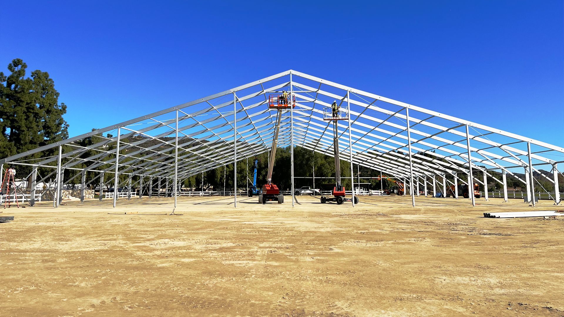 A large metal structure is being built in a dirt field.