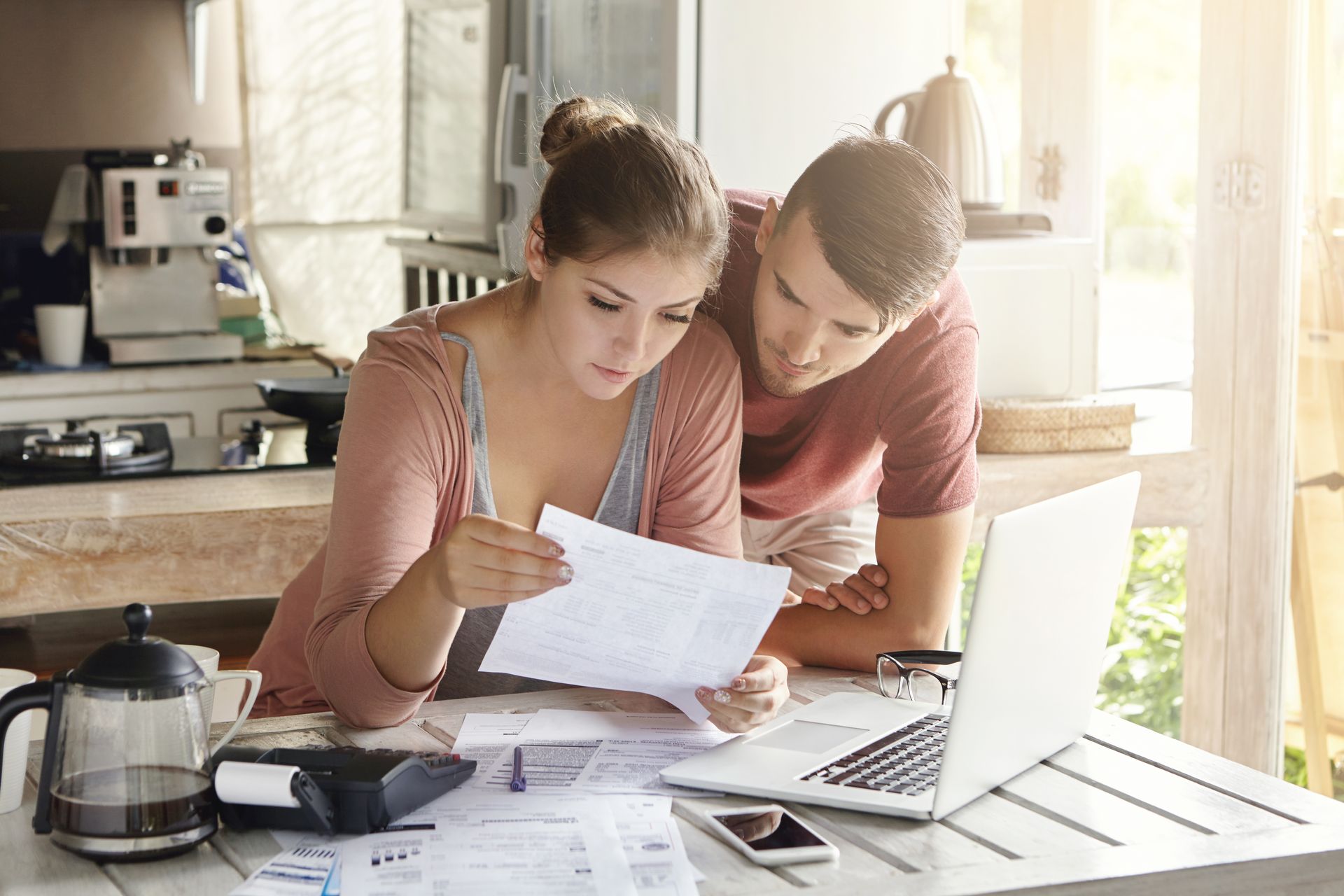 Couple reviewing documents at a table with a laptop, calculator, and phone. They look concerned.