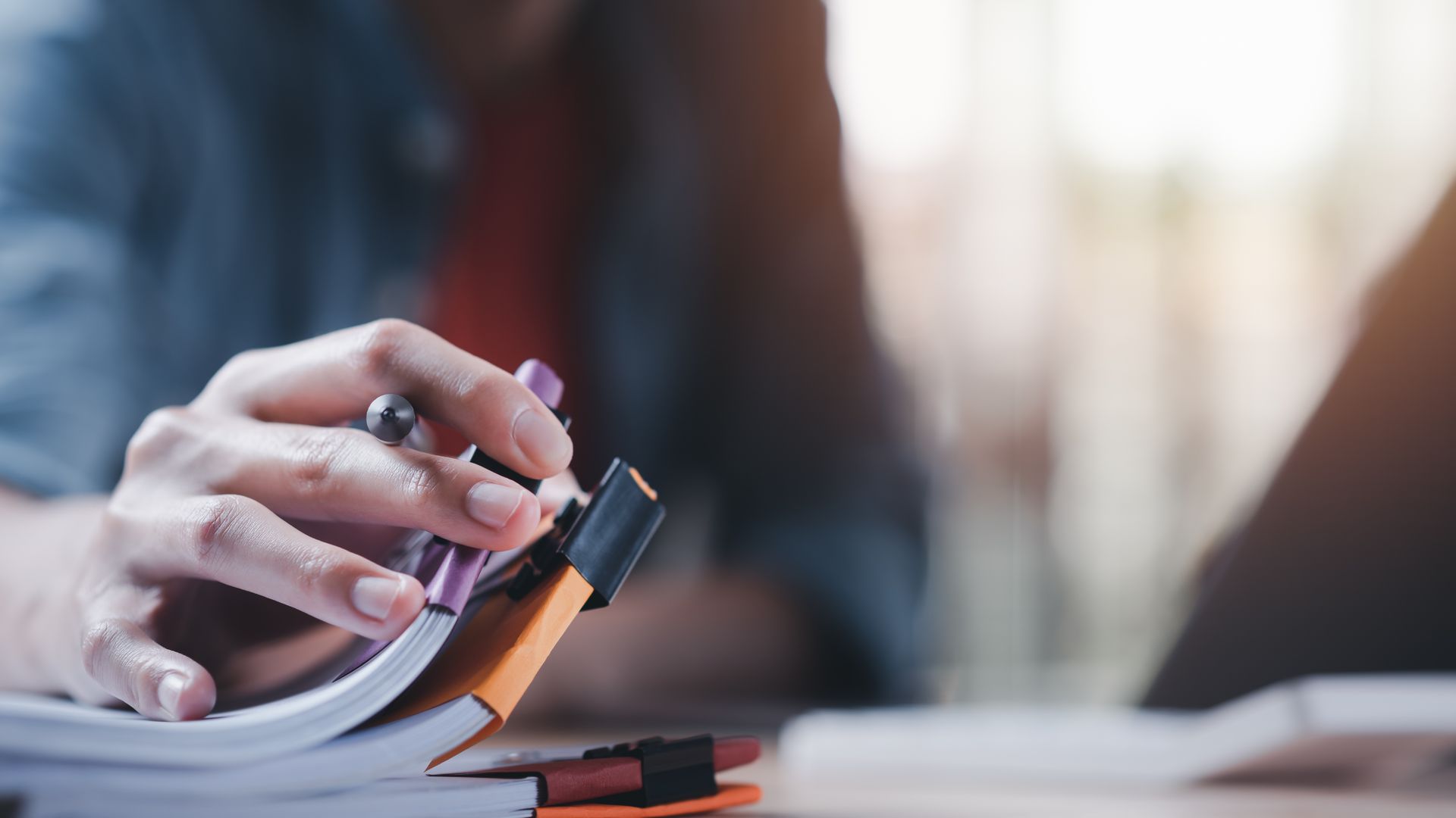 Person's hand using a binder clip to hold open a notebook with pen.