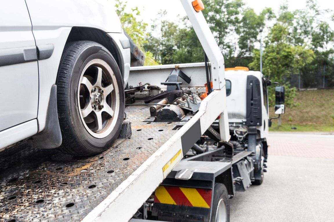 Car on a tow truck flatbed after a roadside accident, with debris visible on the ramp.
