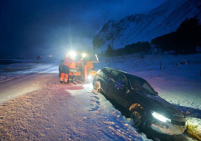 Tow truck pulling a black car from deep snow at night on a snowy roadside