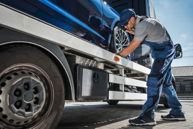 Mechanic inspecting a blue truck’s undercarriage beside a garage loading area